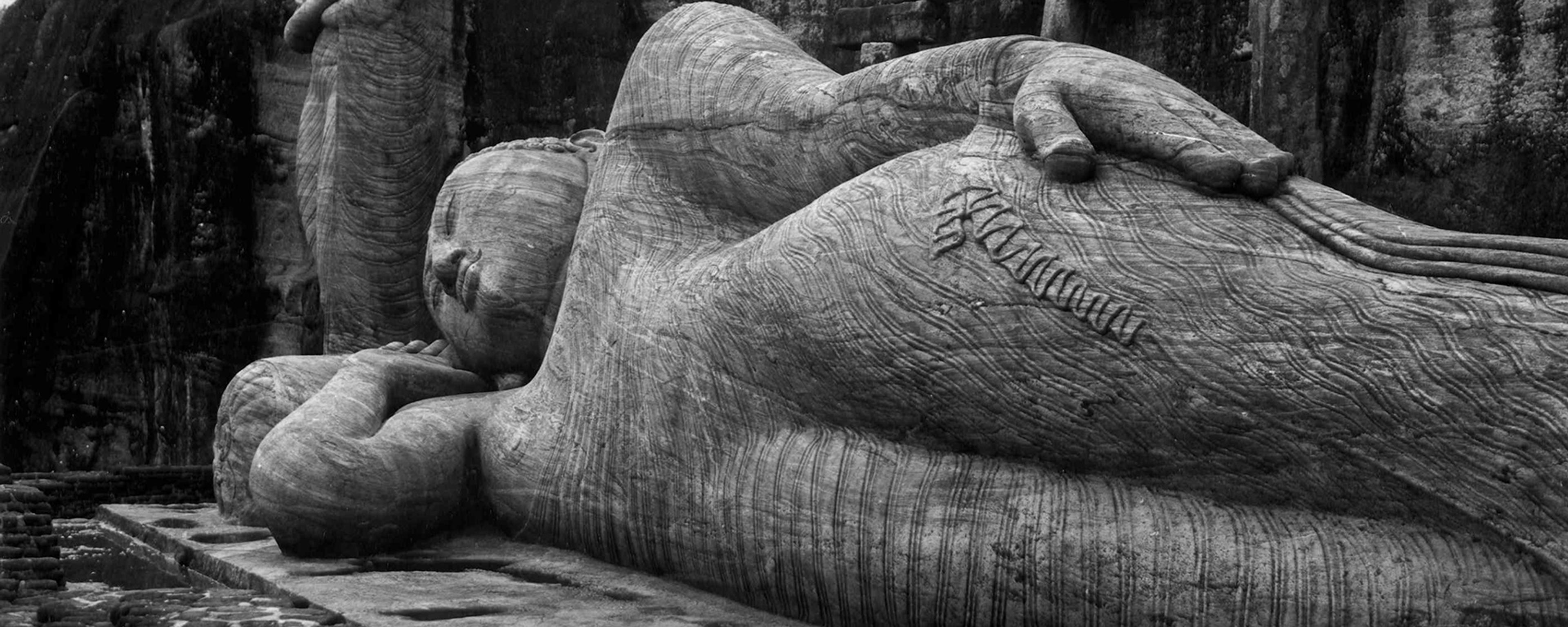 Ancient stone statues depicting a standing and a reclining Buddha against a natural rock backdrop.