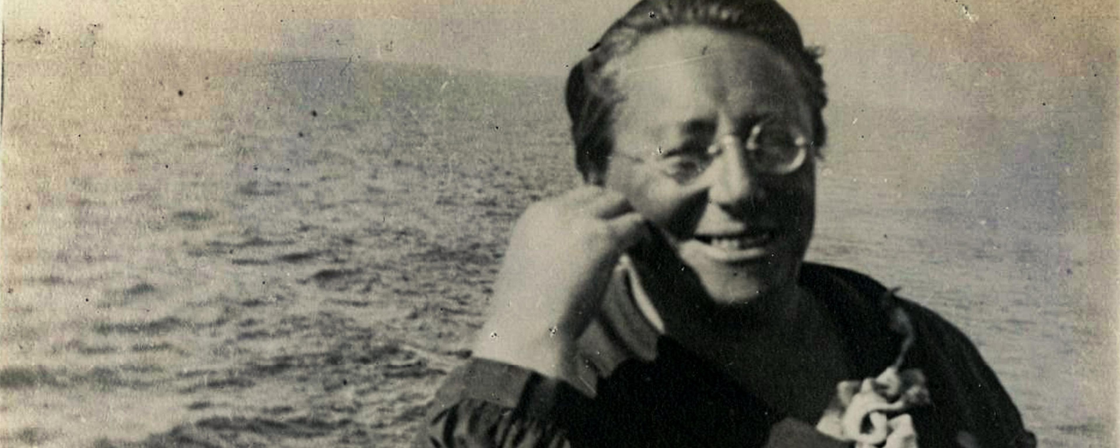 Old black and white photo of a smiling person on a boat with the sea in the background.
