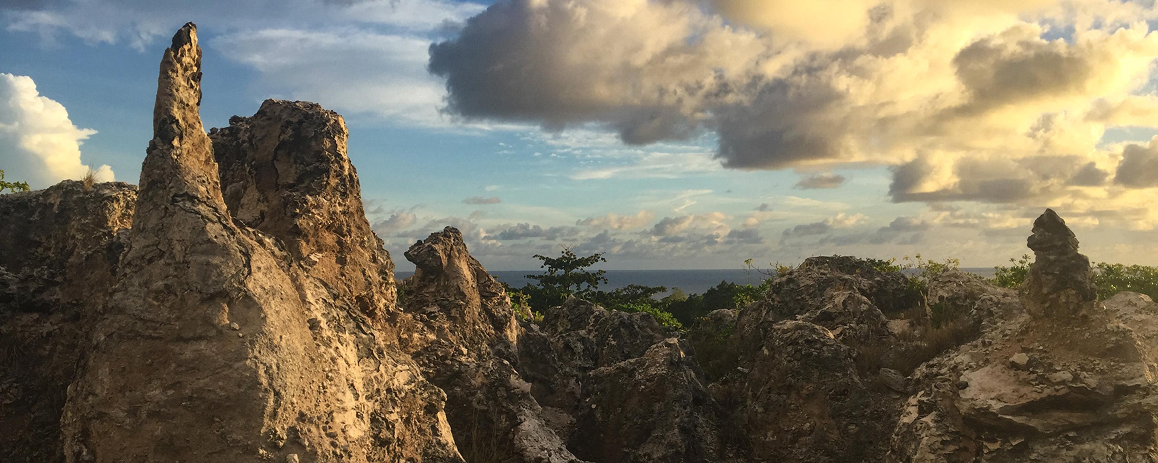 Photo of rugged limestone formations at sunset with a partly cloudy sky and sea visible in the background.