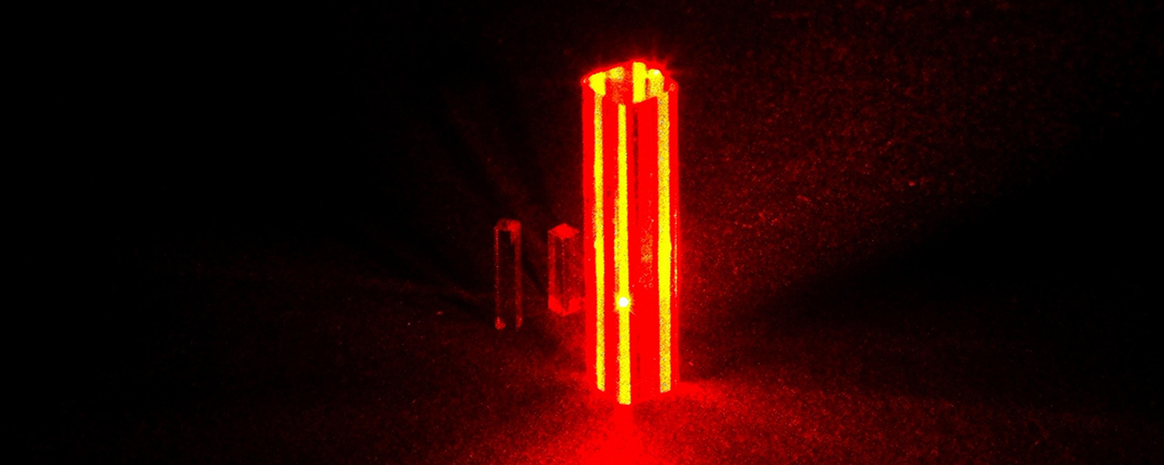 Photo of three vertical beams of red laser light in a dark room creating a glowing effect on the floor.
