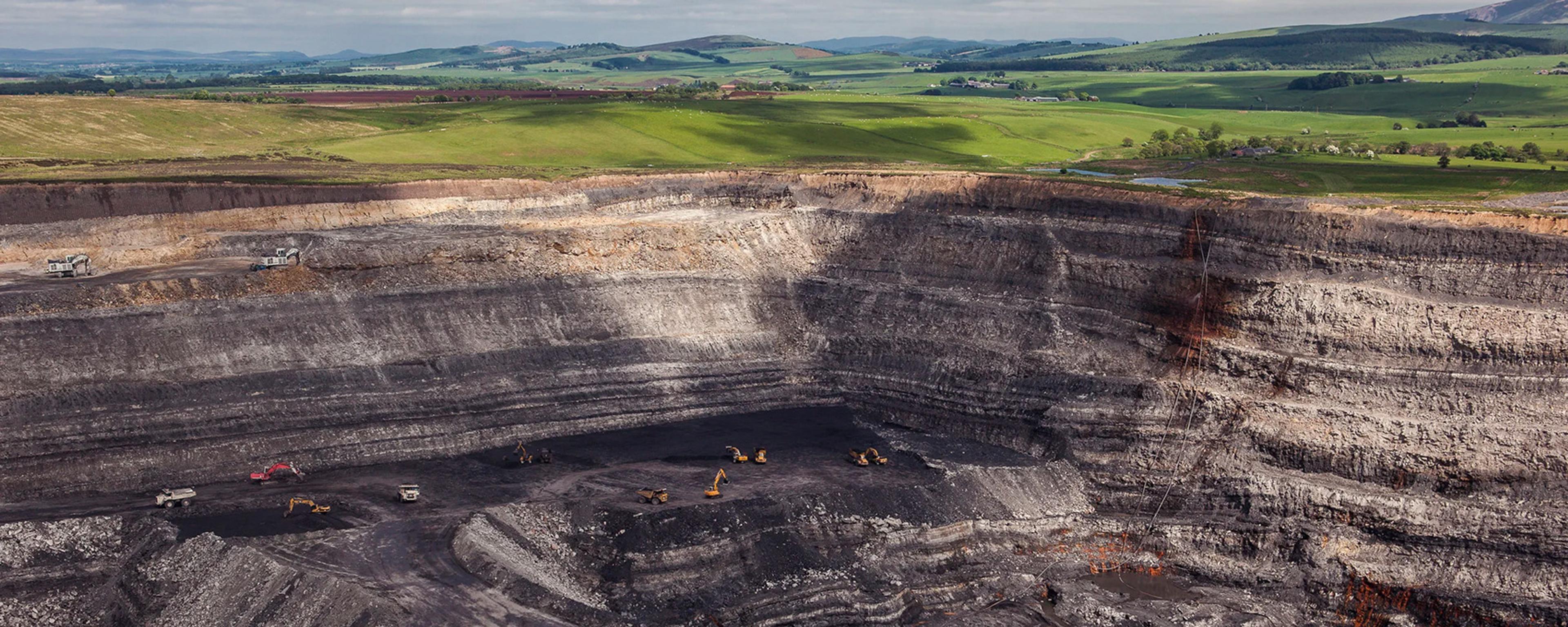 A vast open-pit coal mine with excavation machinery surrounded by green hills.