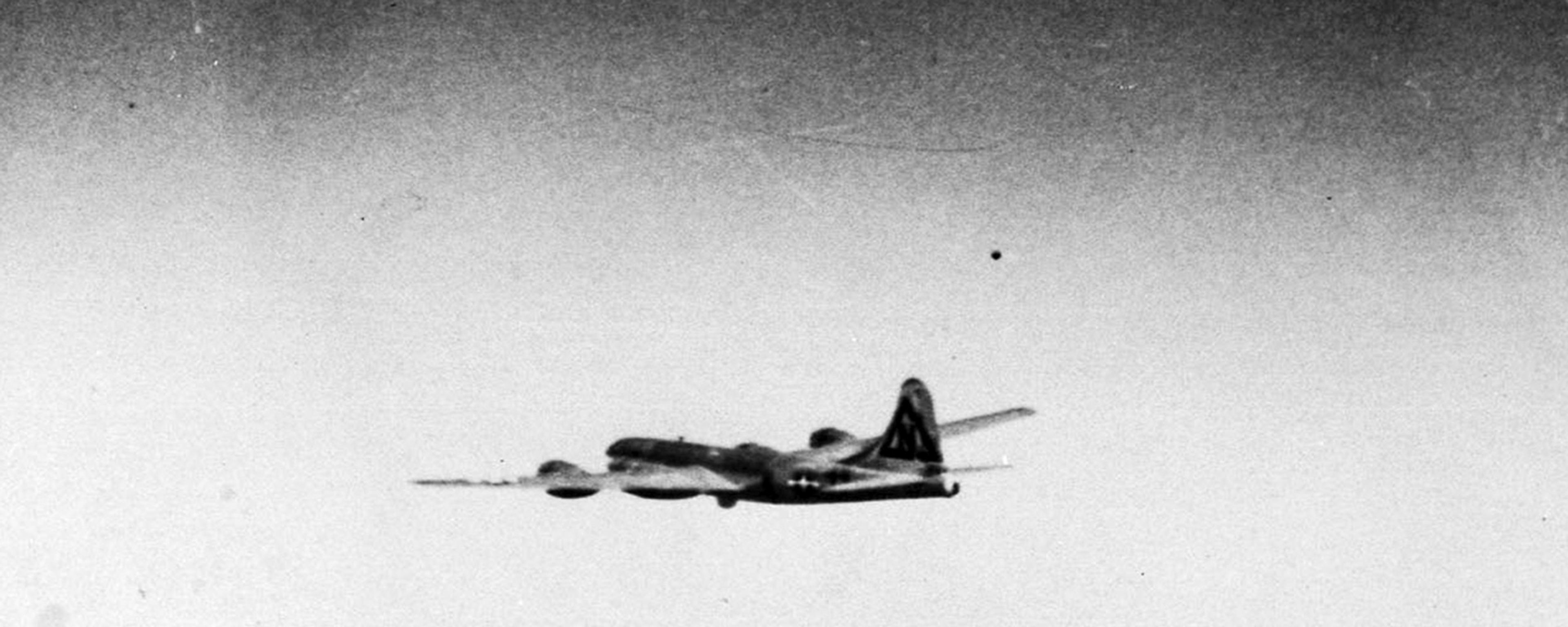 Black and white photo of a vintage propeller aircraft flying in a clear sky.