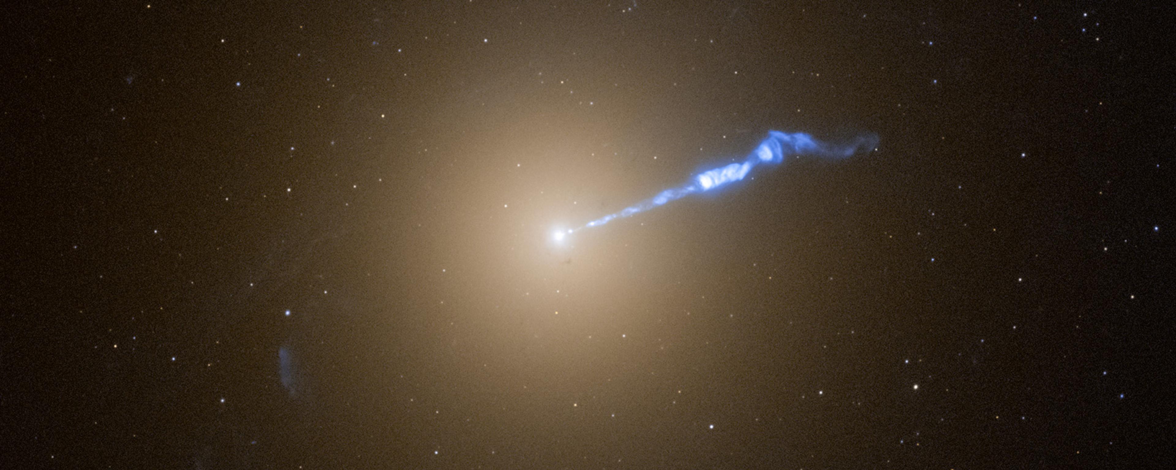 Photo of a galaxy with a bright centre emitting a blue jet of energy against a background of numerous stars in space.