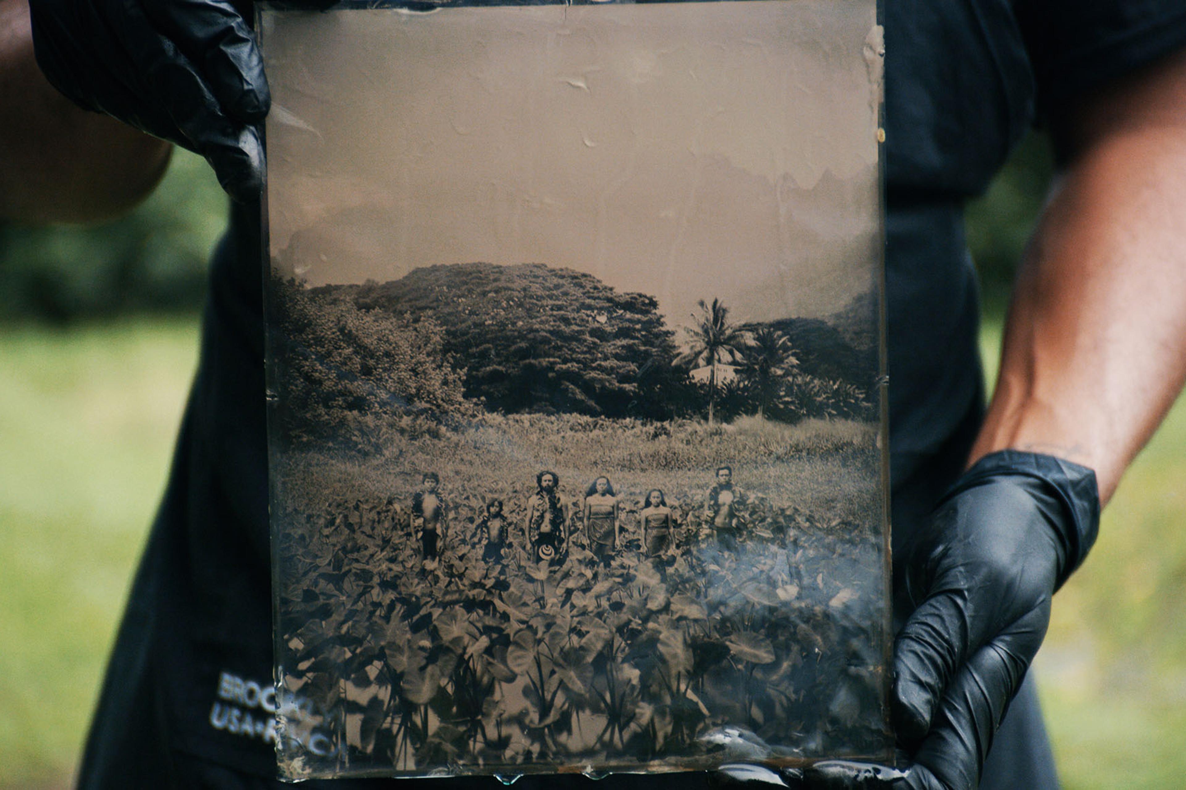 Person holding a vintage photograph featuring six people standing in a field with trees in the background.