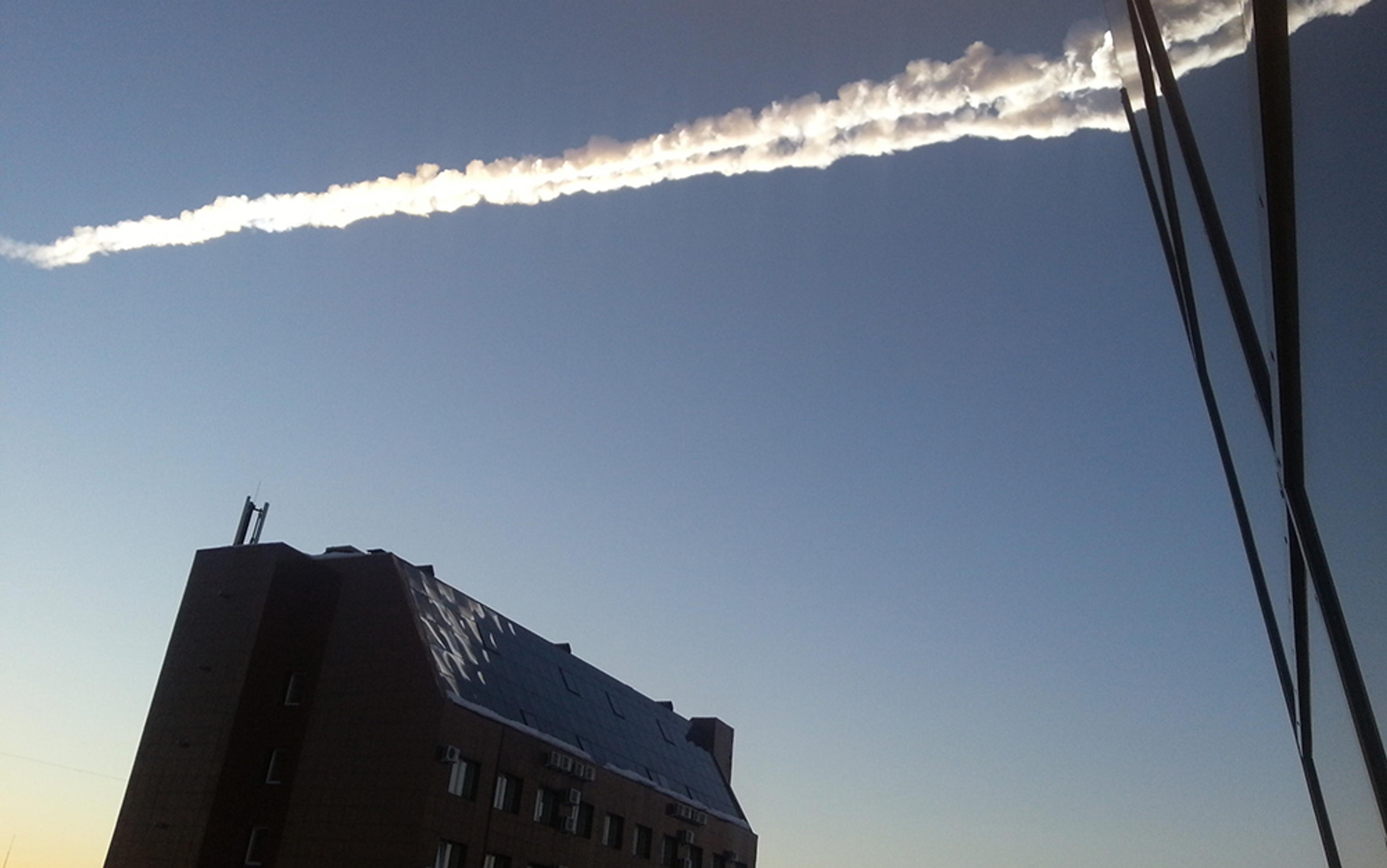 The sky with a vapour trail over a building. The scene includes part of a reflective glass building on the right side.