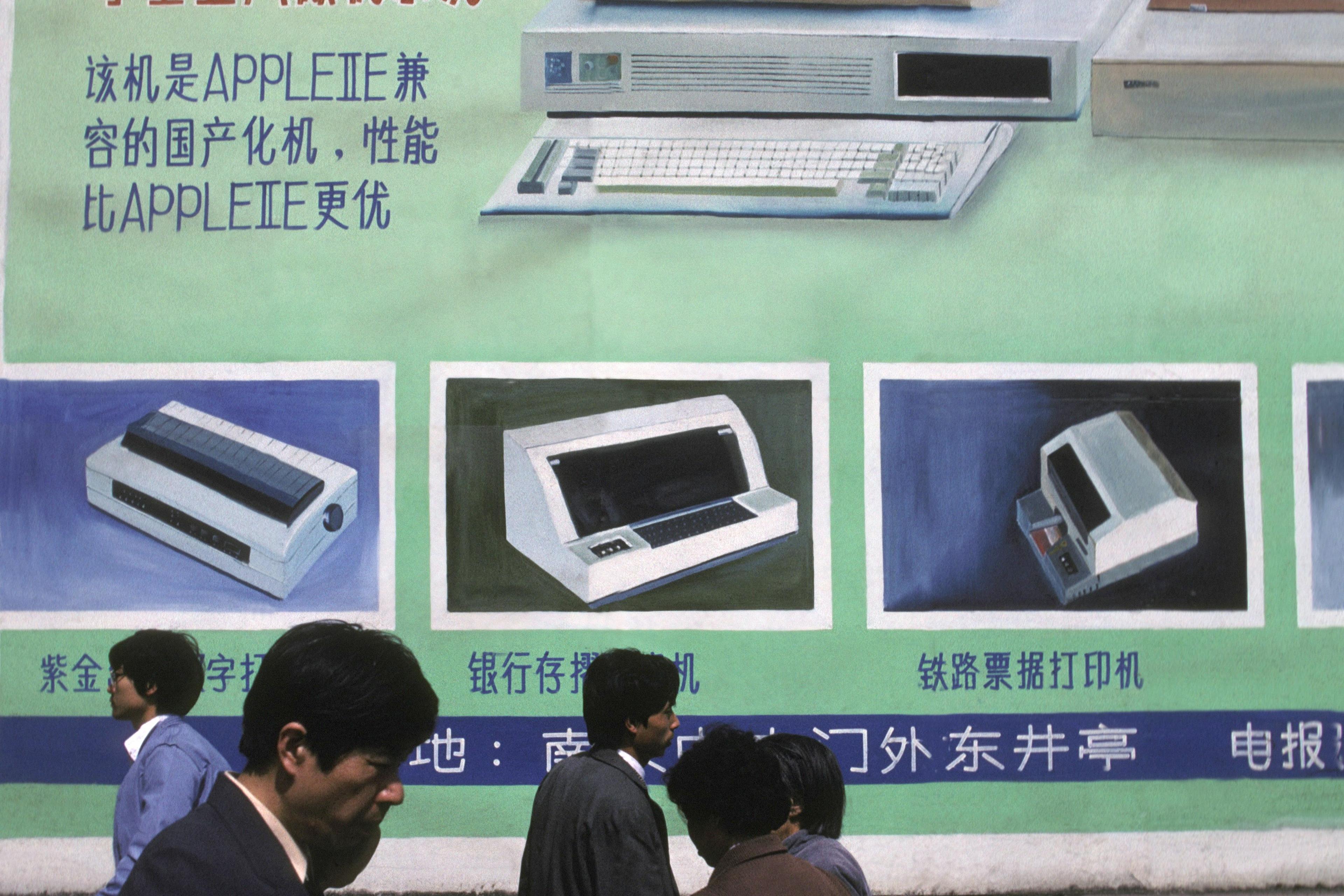 Photo of people walking past a wall with a retro computer advertisement in Chinese featuring a computer and peripherals.