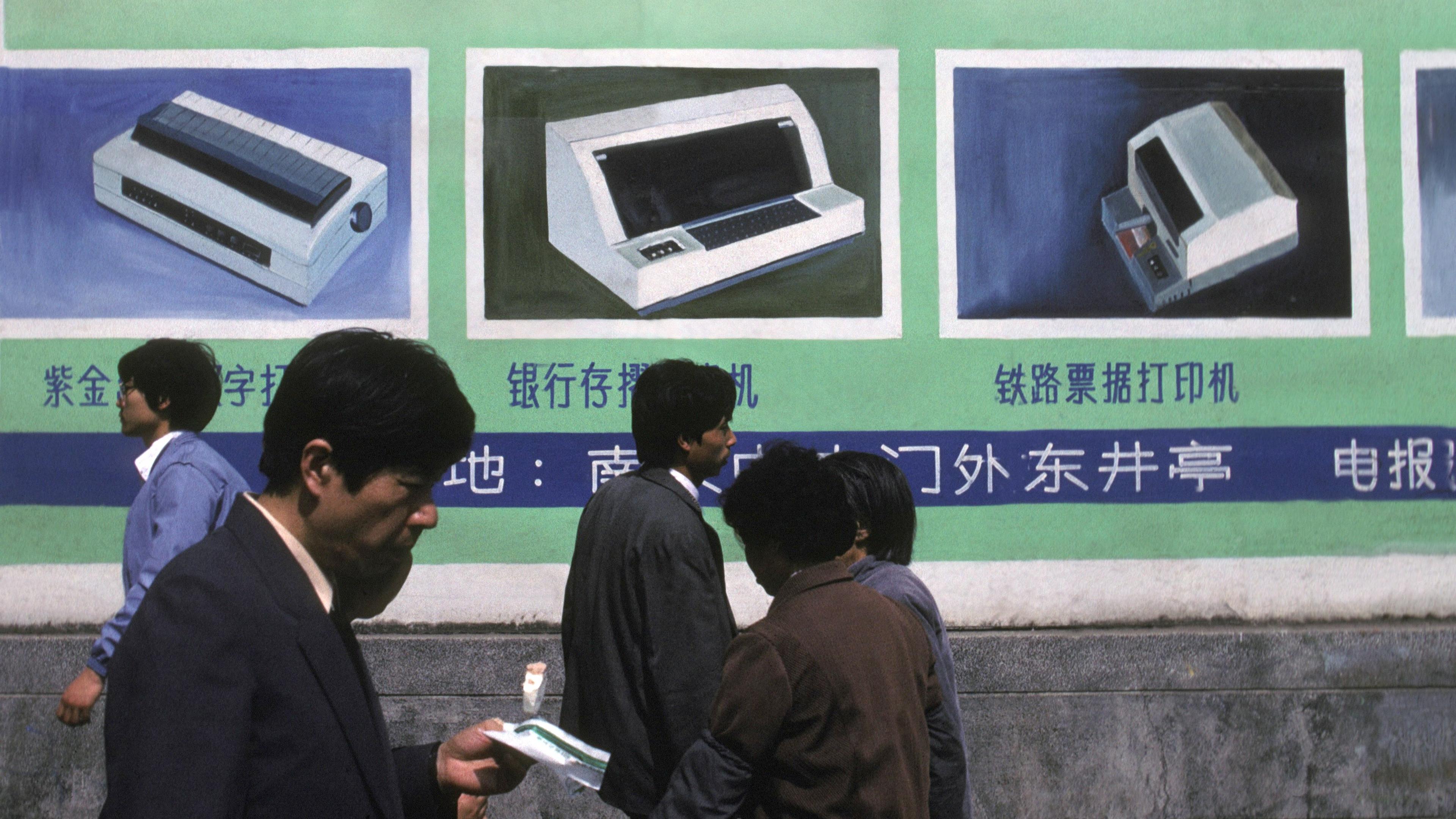 Photo of people walking past a wall with a retro computer advertisement in Chinese featuring a computer and peripherals.