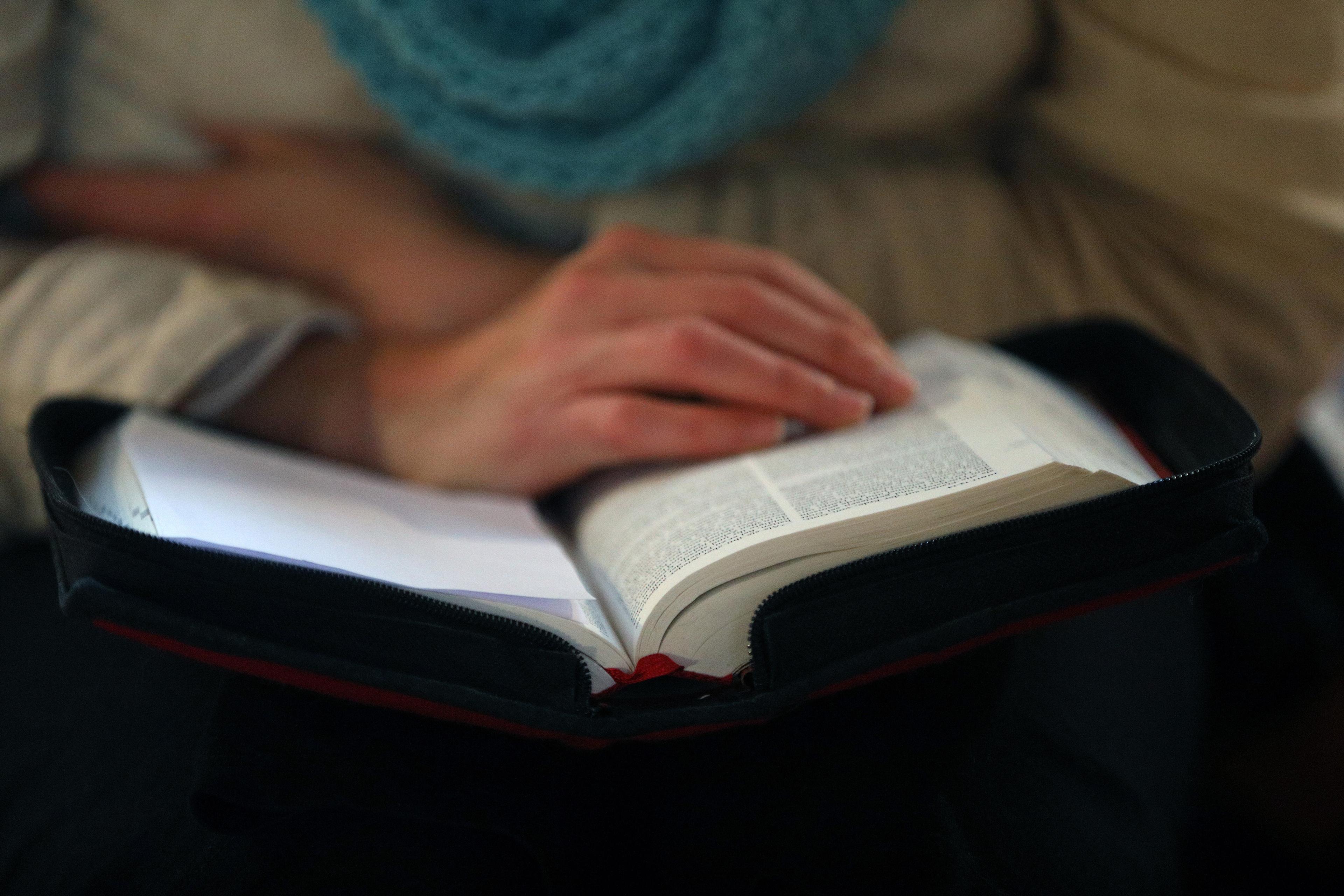 A person reading an open book with a blue scarf and hands resting on the pages in a calm setting.