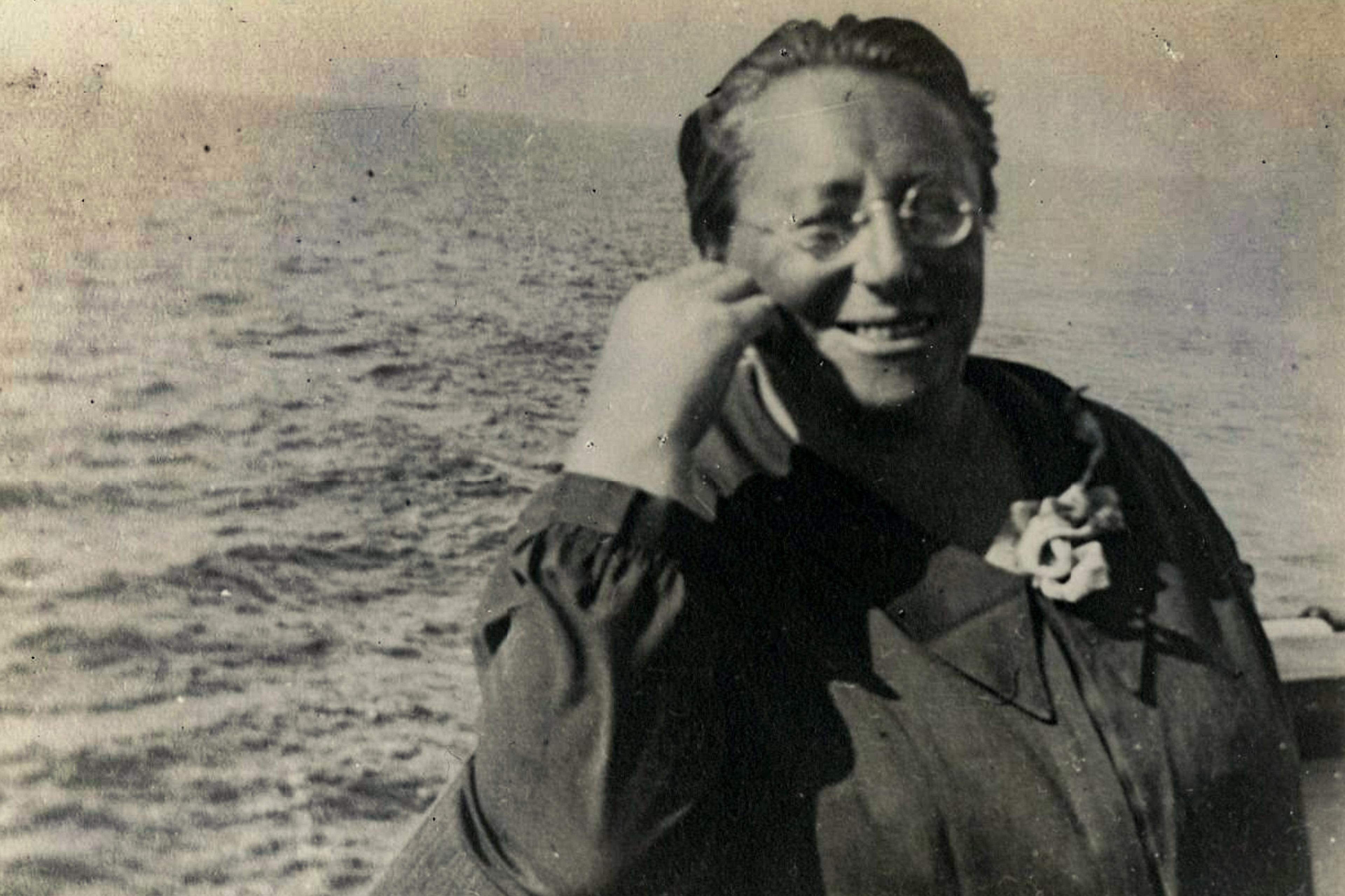 Old black and white photo of a smiling person on a boat with the sea in the background.