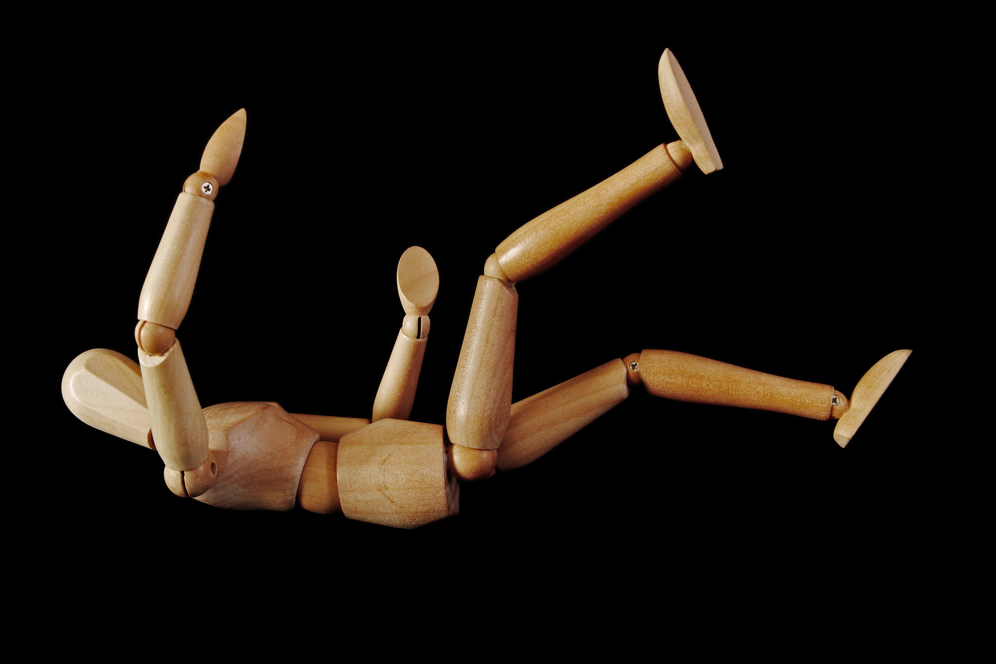 Photo of a wooden artist mannequin lying on its back with limbs bent against a black background.