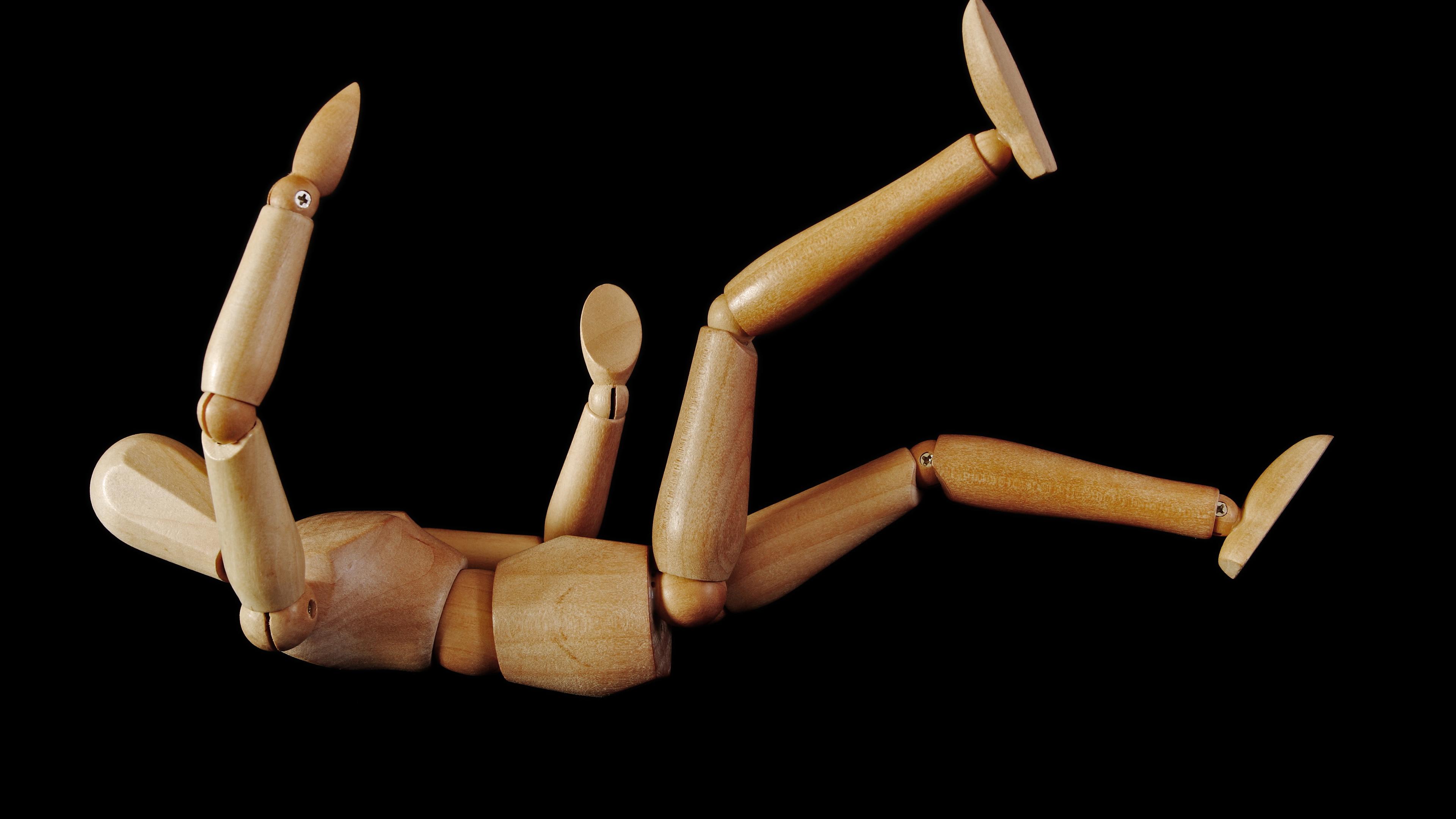 Photo of a wooden artist mannequin lying on its back with limbs bent against a black background.