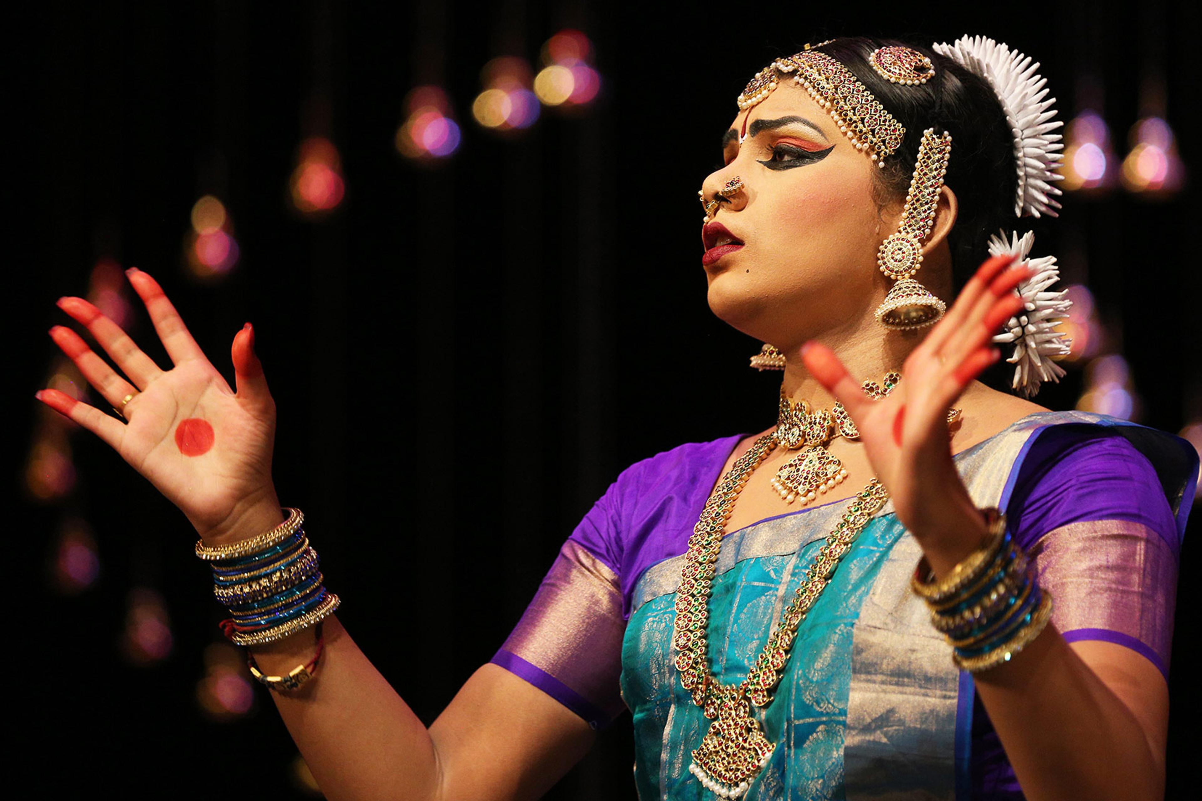 A dancer in traditional Indian dress performs on stage against a black background