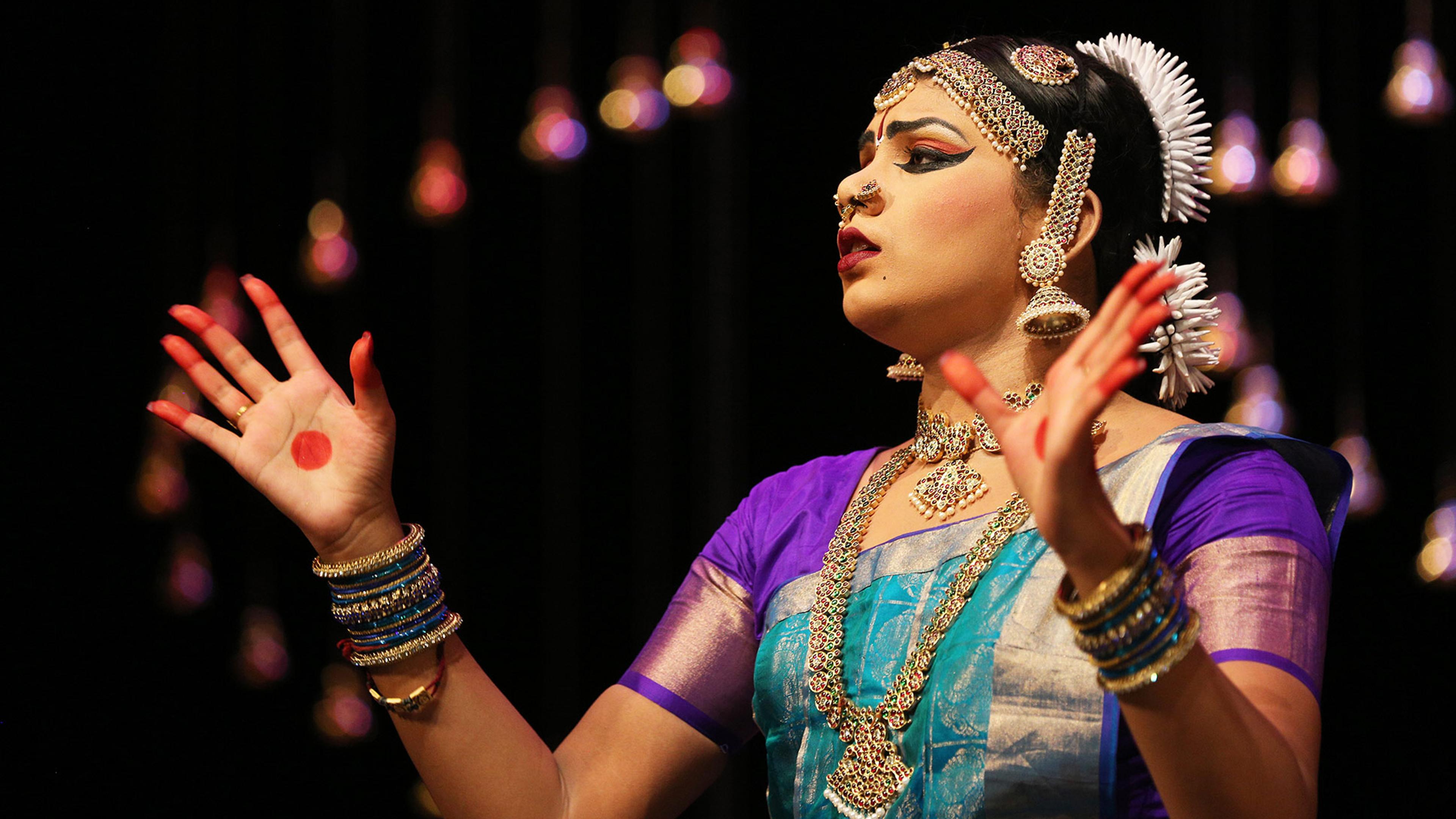 A dancer in traditional Indian dress performs on stage against a black background