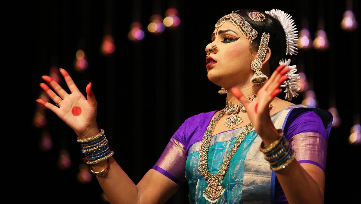 A dancer in traditional Indian dress performs on stage against a black background