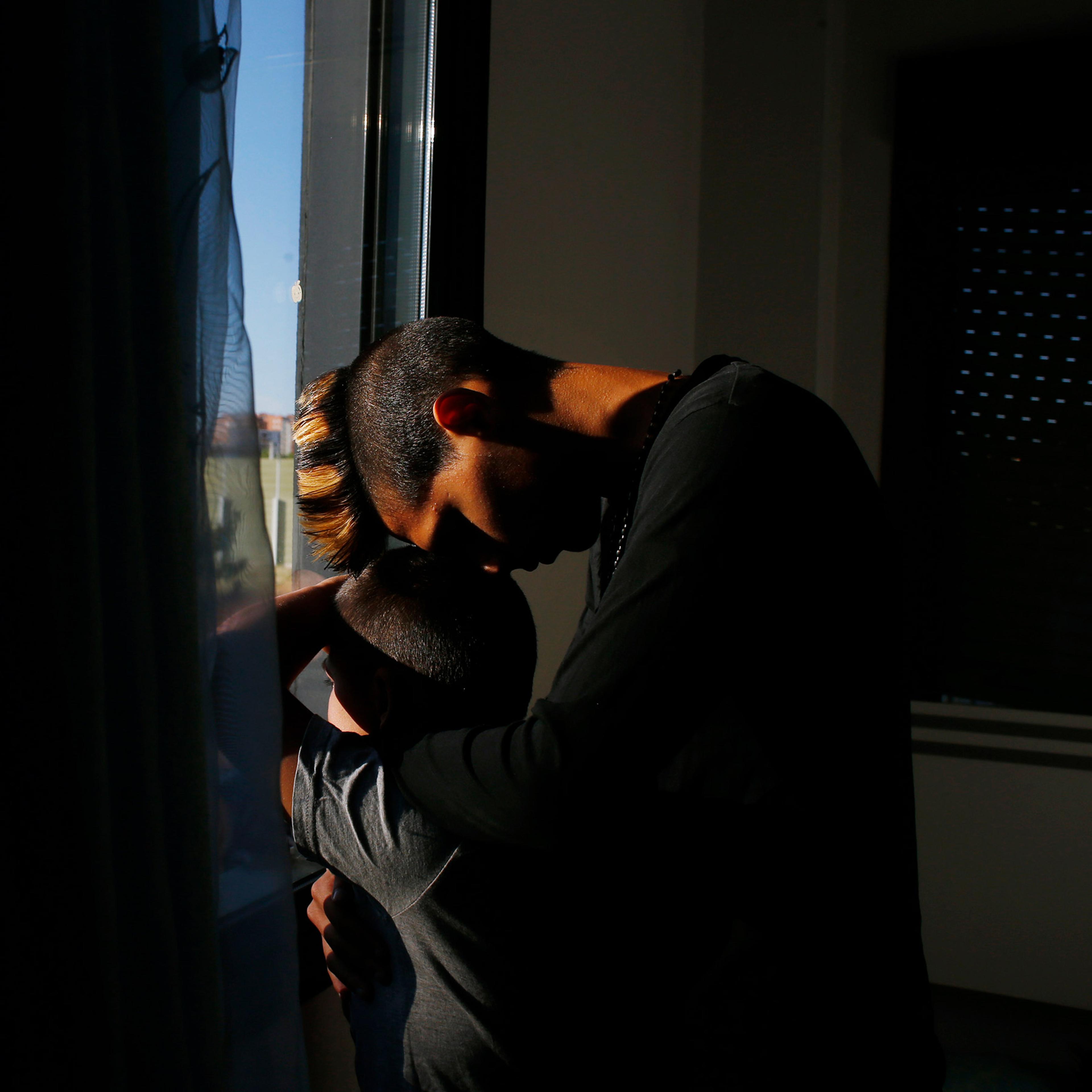 A man hugs his son in the light of a sunny day coming through a window in a darkened room