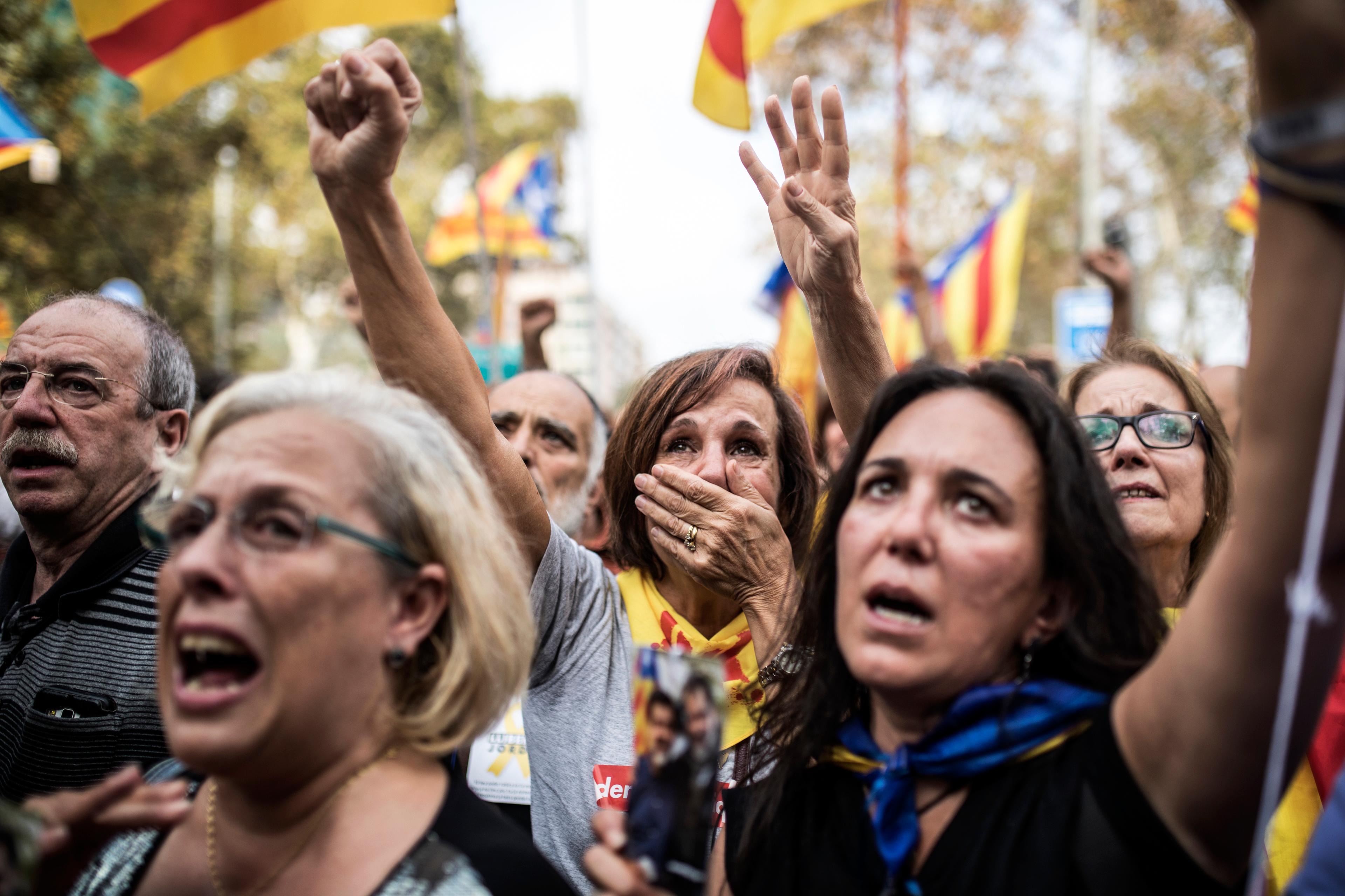 Photo of emotional protesters raising hands and holding Catalan flags in a crowd during a demonstration.