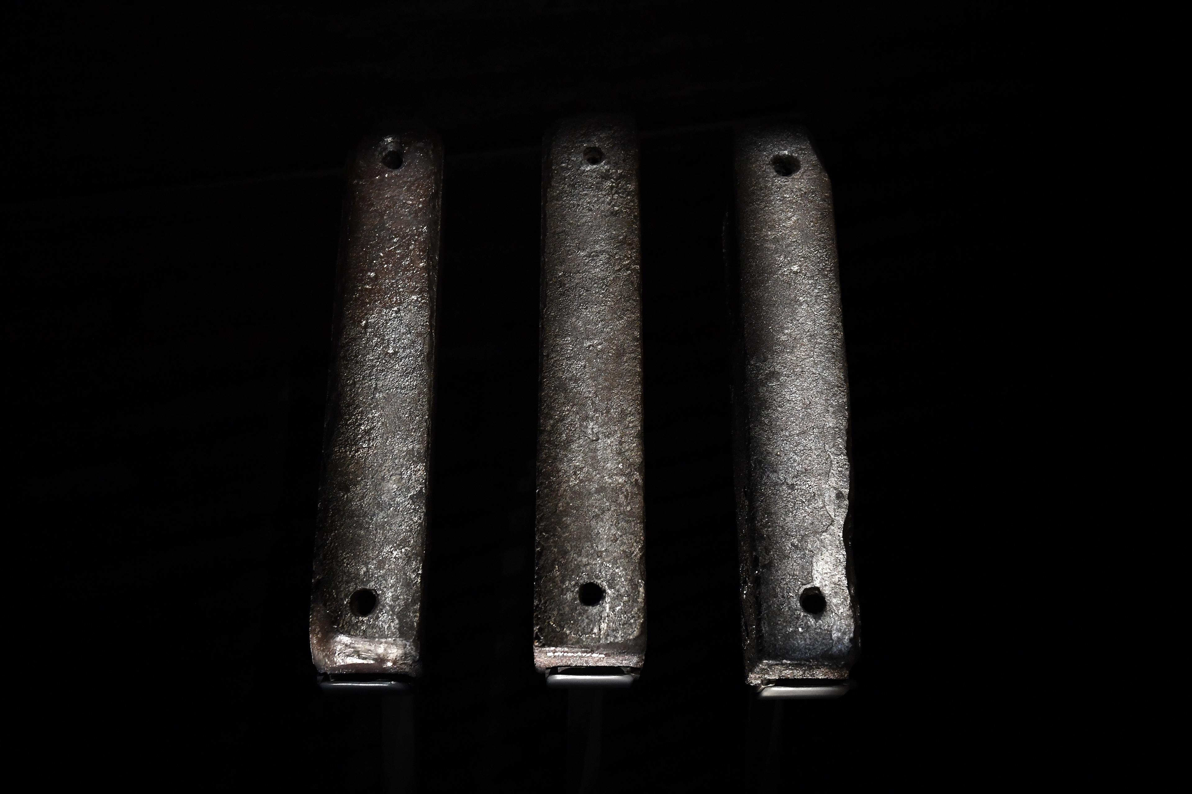 Photo of three aged metal bars with small holes, standing vertically against a dark background.