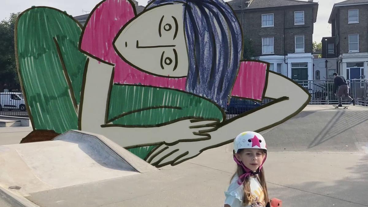 A young girl in a helmet and with a skateboard stands in a skatepark. Behind her is a hand-drawn reclining figure.