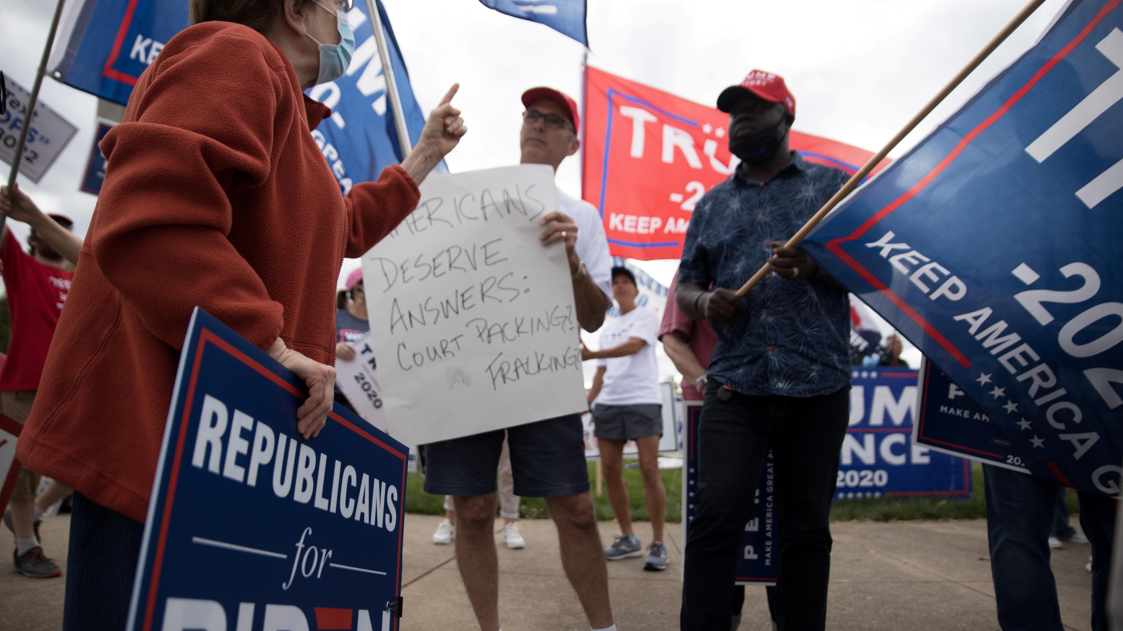 Photo of a political protest with people holding Biden and Trump signs, one wearing a mask and holding a “Republicans for Biden” sign.