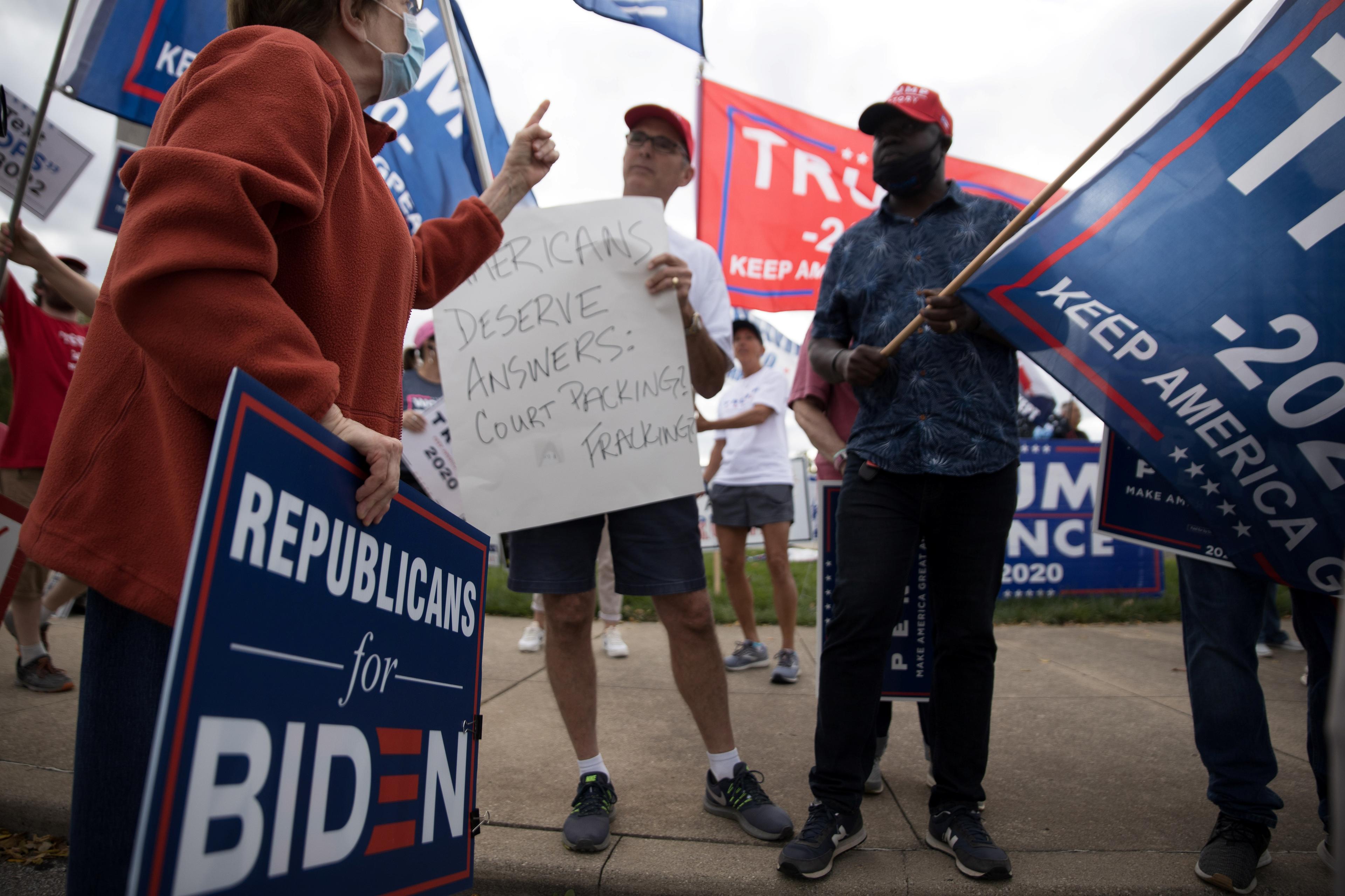 Photo of a political protest with people holding Biden and Trump signs, one wearing a mask and holding a “Republicans for Biden” sign.