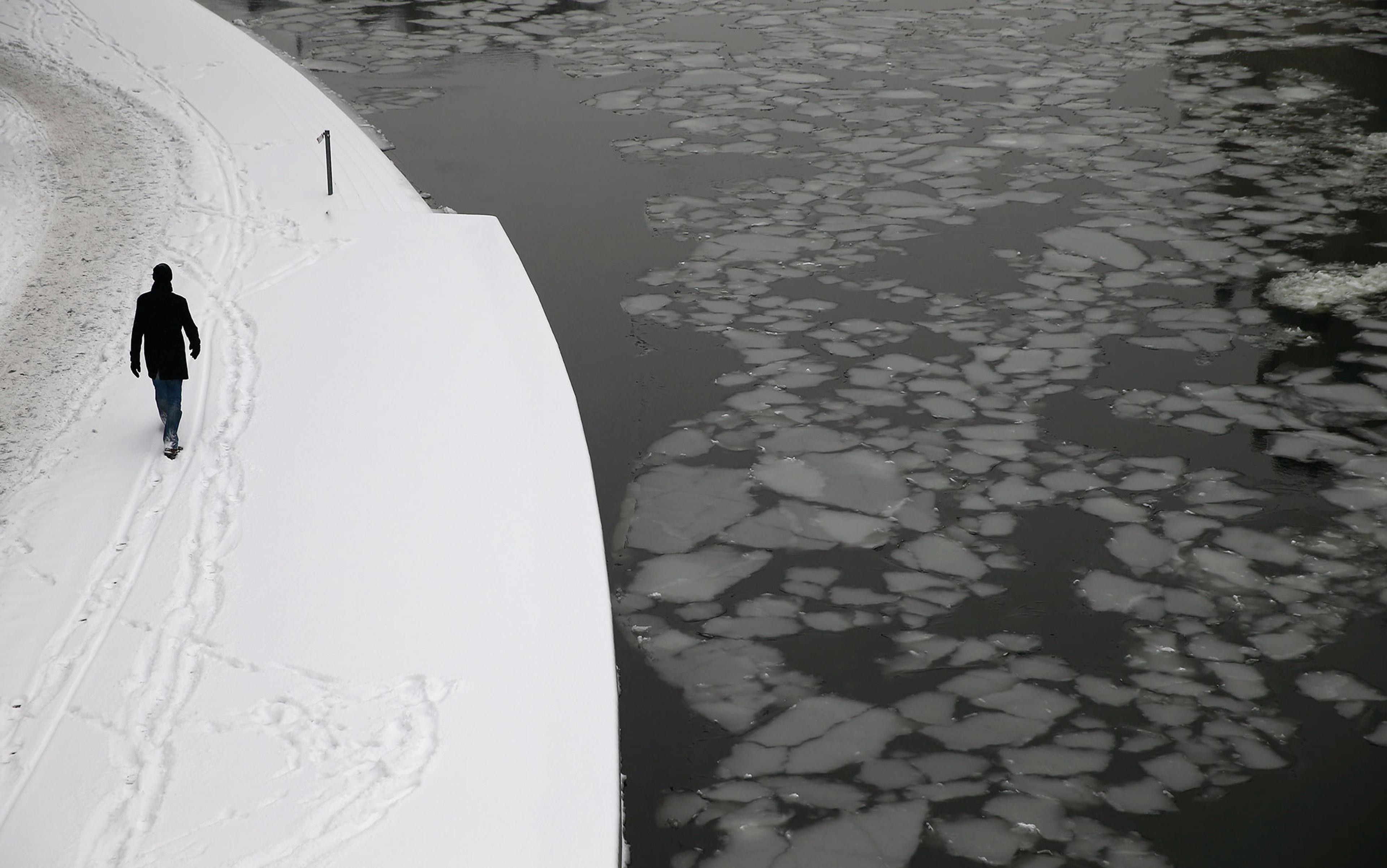 A photo of a person walking on a snowy path beside an icy river with floating ice chunks.