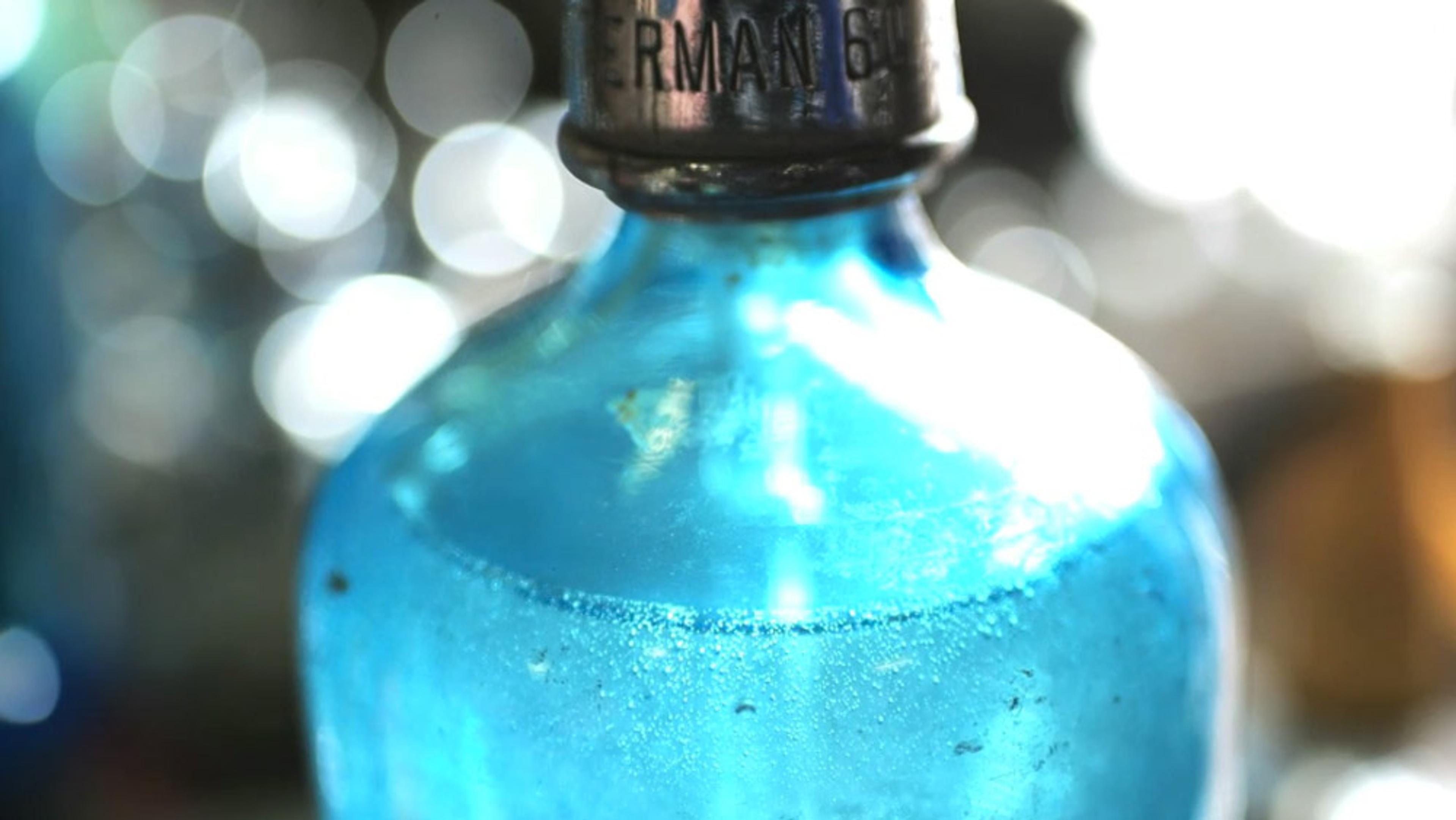 Close-up of a vintage blue glass bottle with a metal cap, featuring bokeh effect lights in the blurred background.