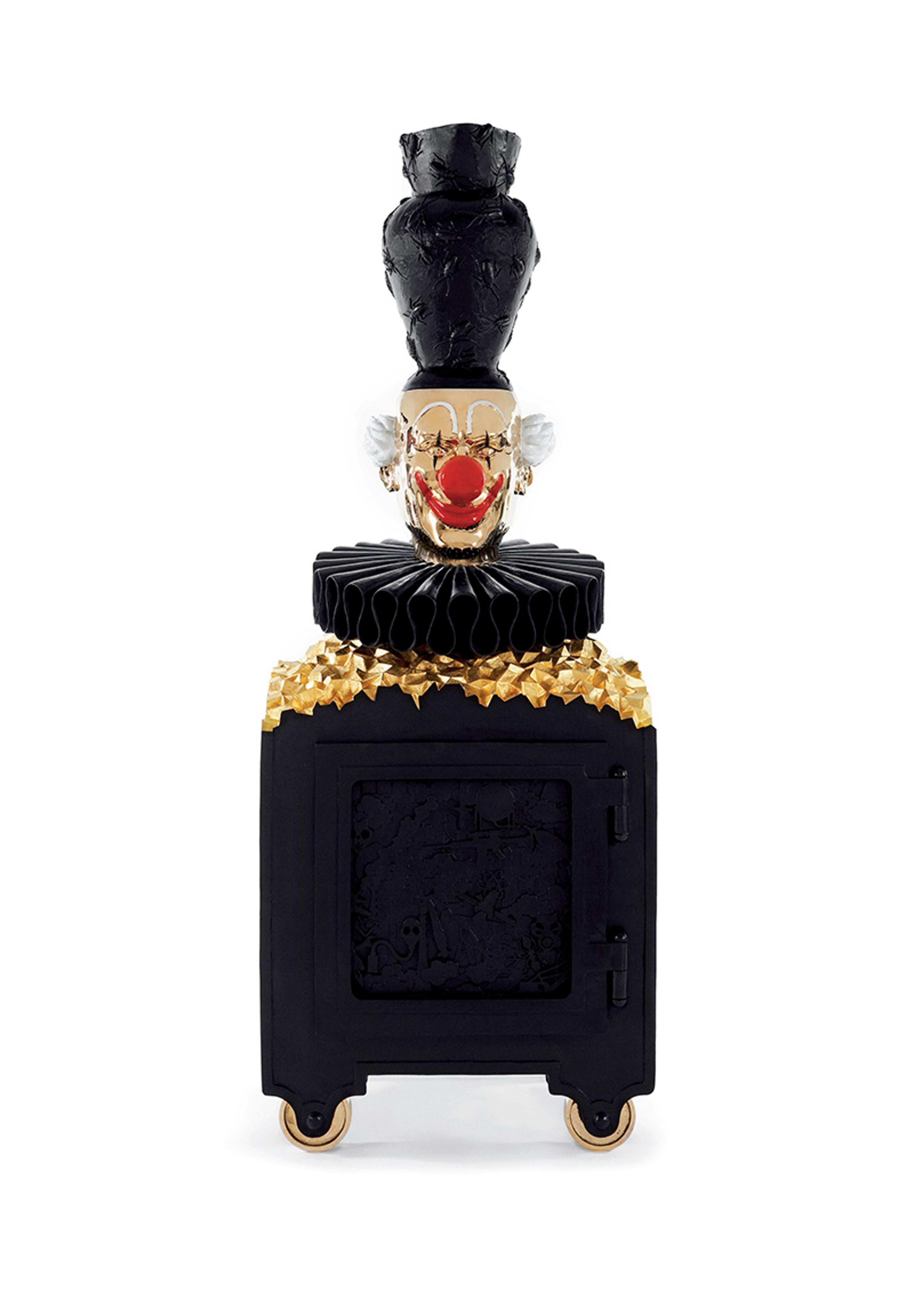 Sculpture with a black, gold and red clown face on top of a black rectangular base, adorned with gold accents and resembling a cabinet.