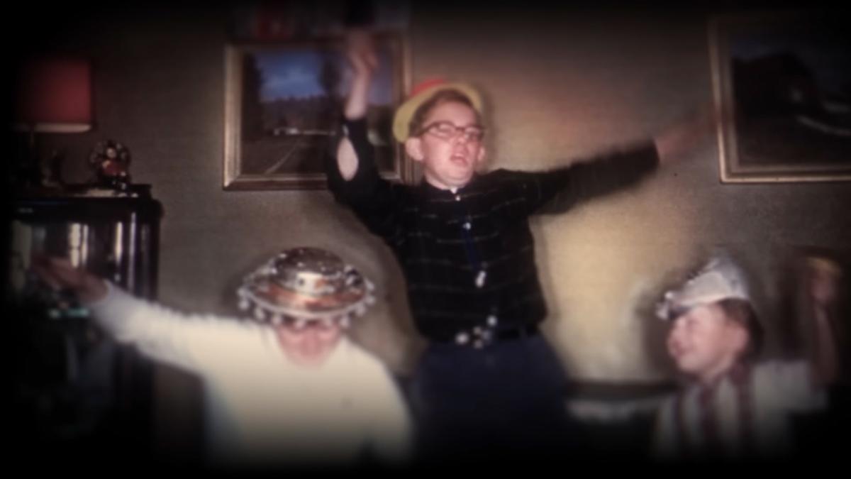 Vintage photo of three children dancing in hats in a living room with framed paintings on the wall.