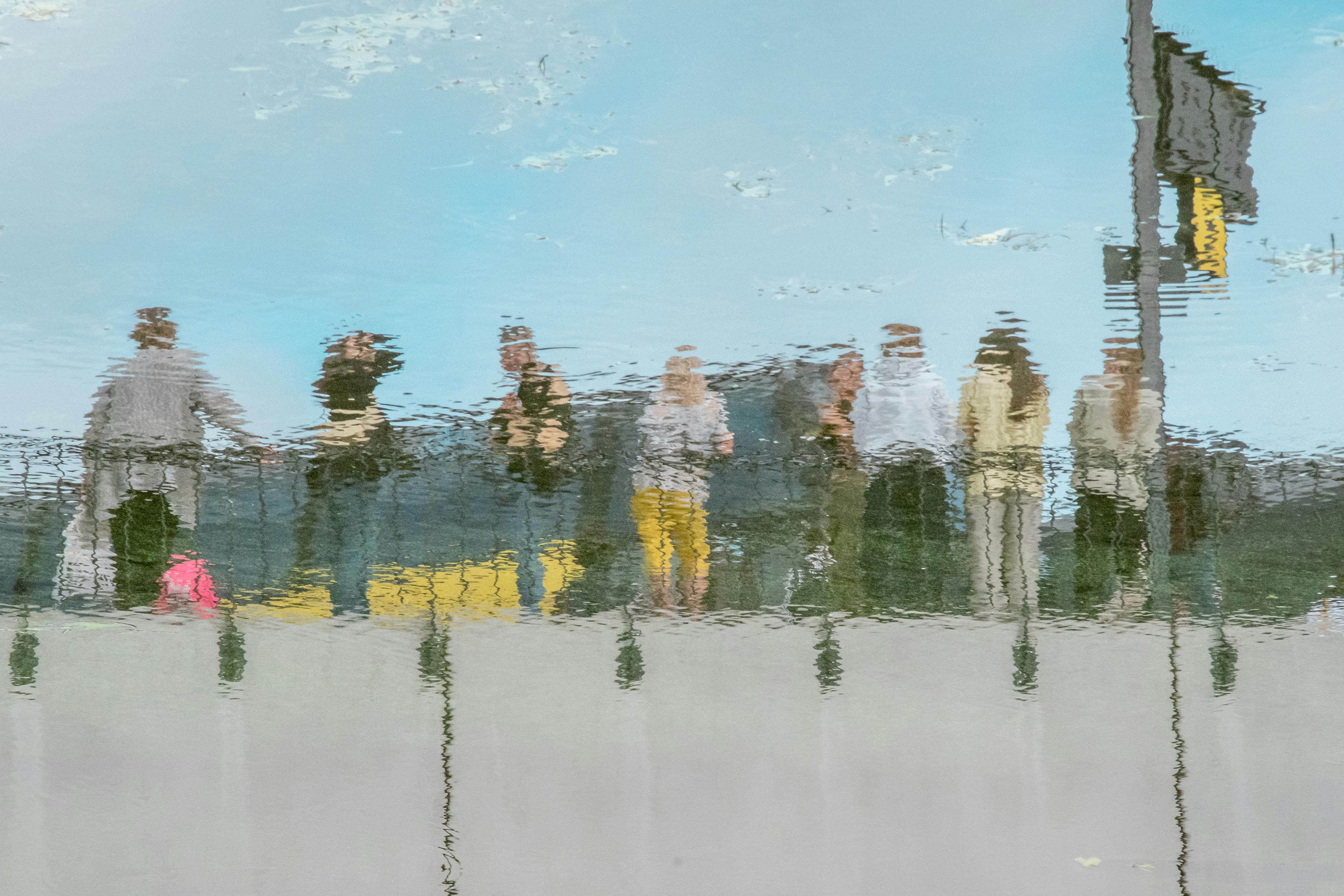 Reflection of a group of people on water surface under blue sky photo distorted by ripples.