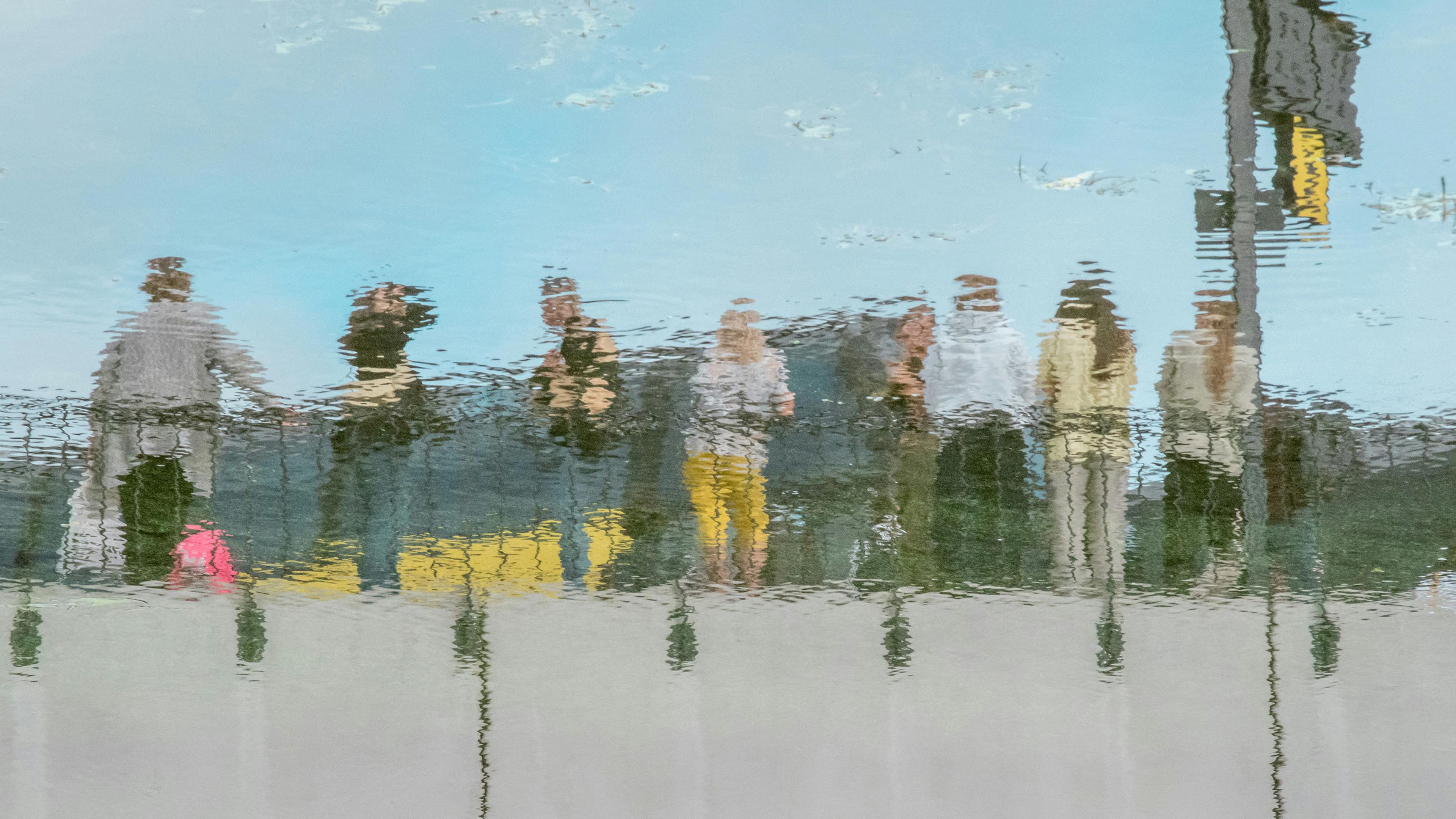 Reflection of a group of people on water surface under blue sky photo distorted by ripples.