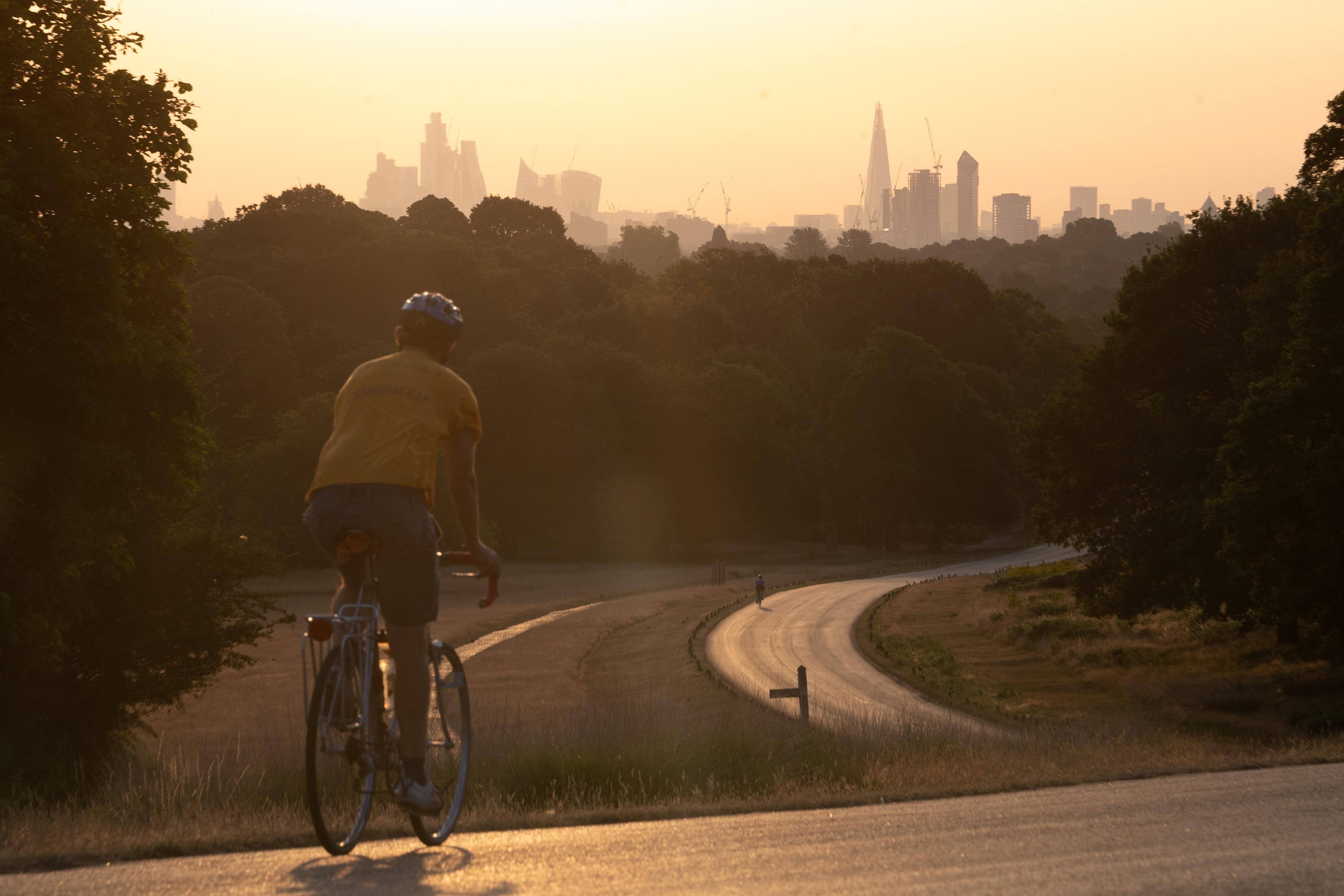 Photo of a cyclist in a yellow shirt on a winding park path at sunset with a city skyline in the background.
