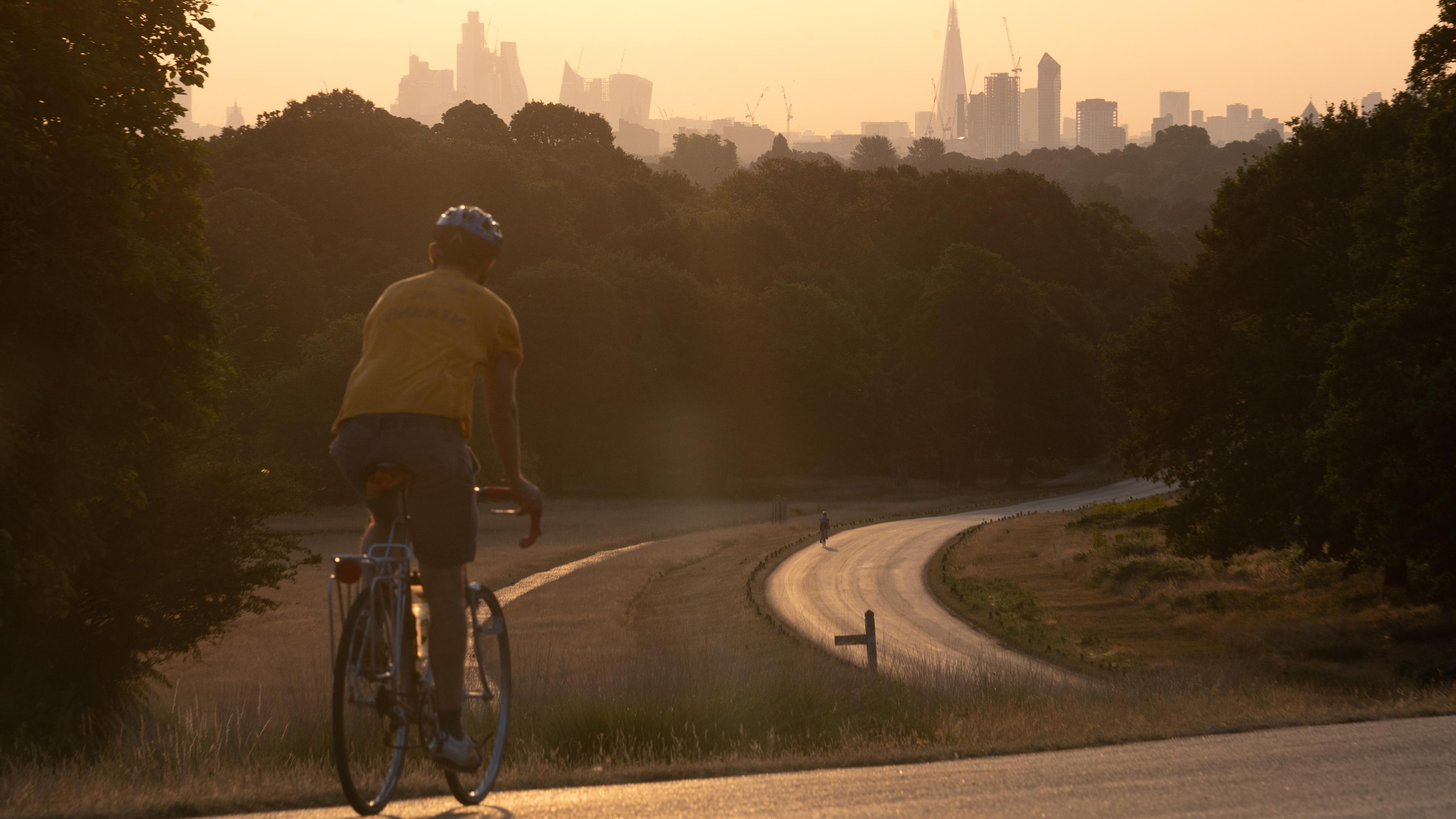 Photo of a cyclist in a yellow shirt on a winding park path at sunset with a city skyline in the background.
