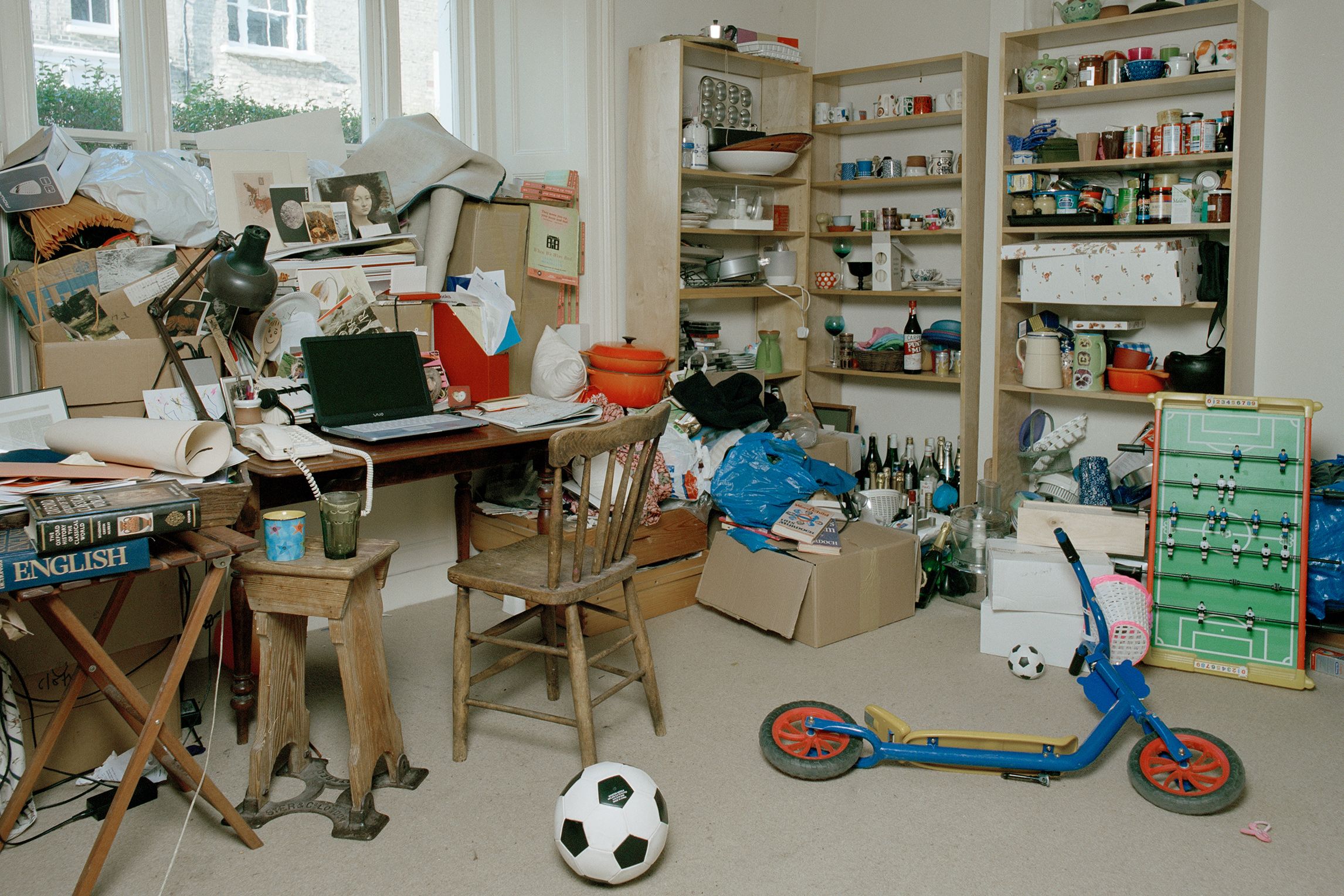 A cluttered room with books, papers, toys and shelves filled with various items, including a table football game.