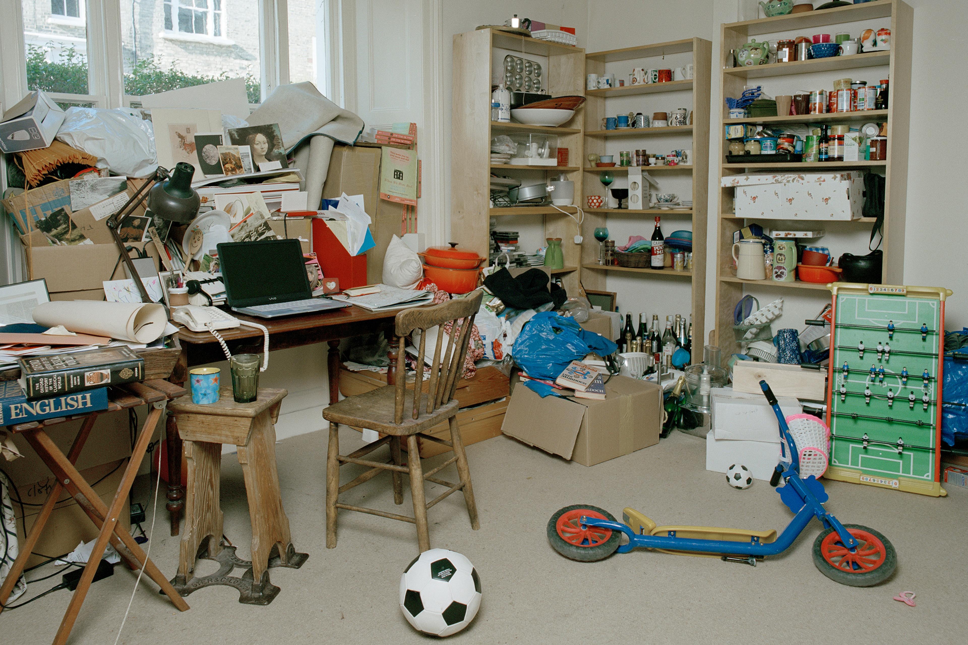A cluttered room with books, papers, toys and shelves filled with various items, including a table football game.