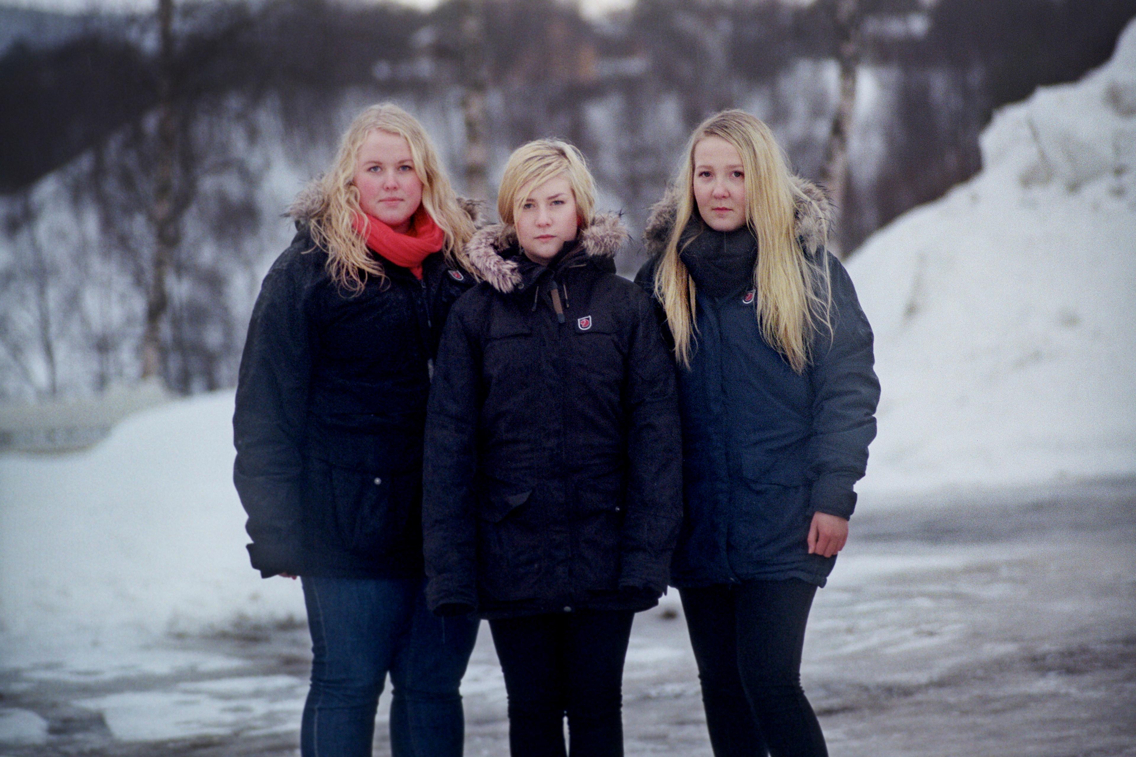 Photo of three people in winter coats standing on a snowy path with bare trees in the background.
