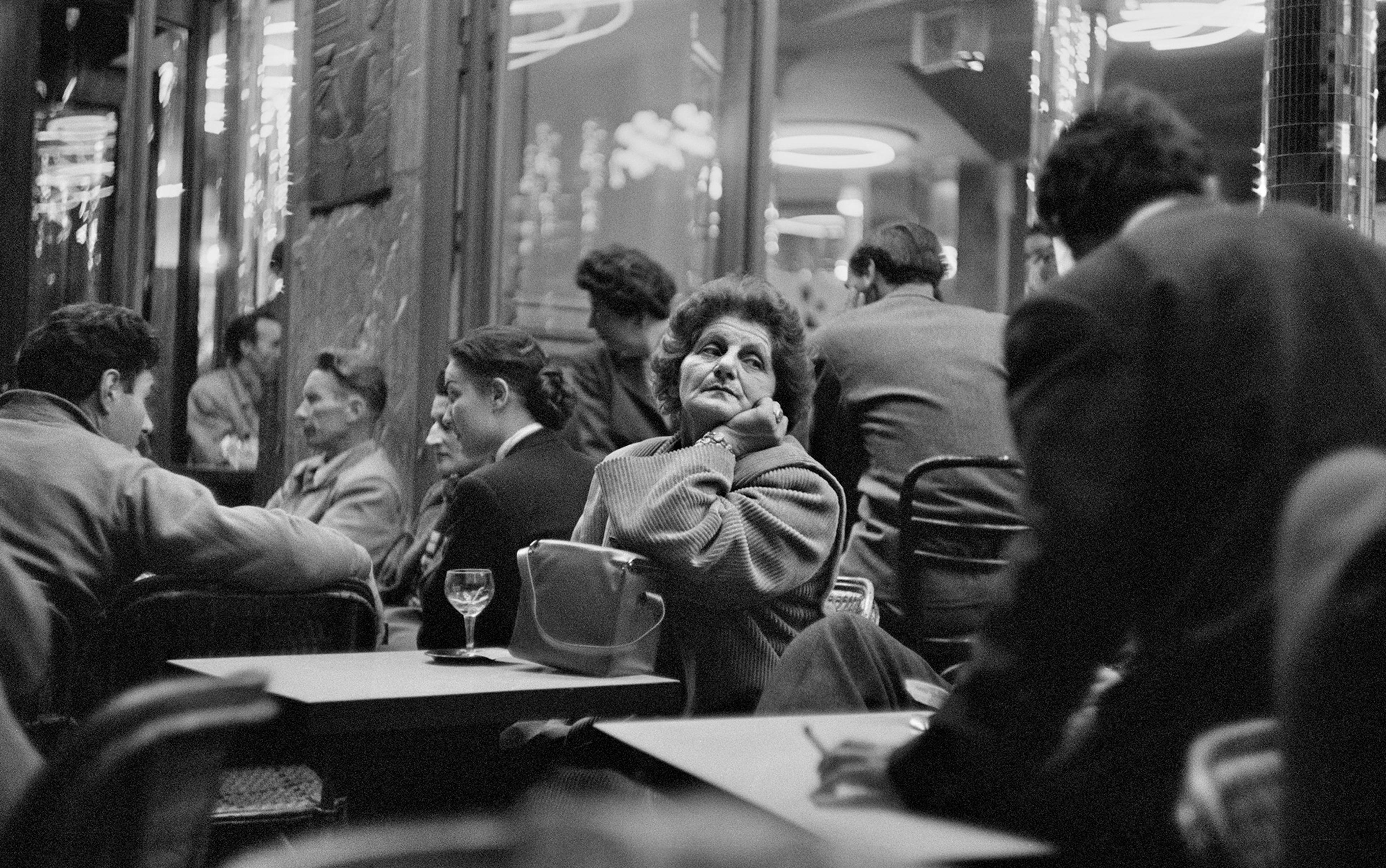 A woman sits alone in a Parisian cafe with a glass of wine, while the neighbouring tables are full of socialising groups