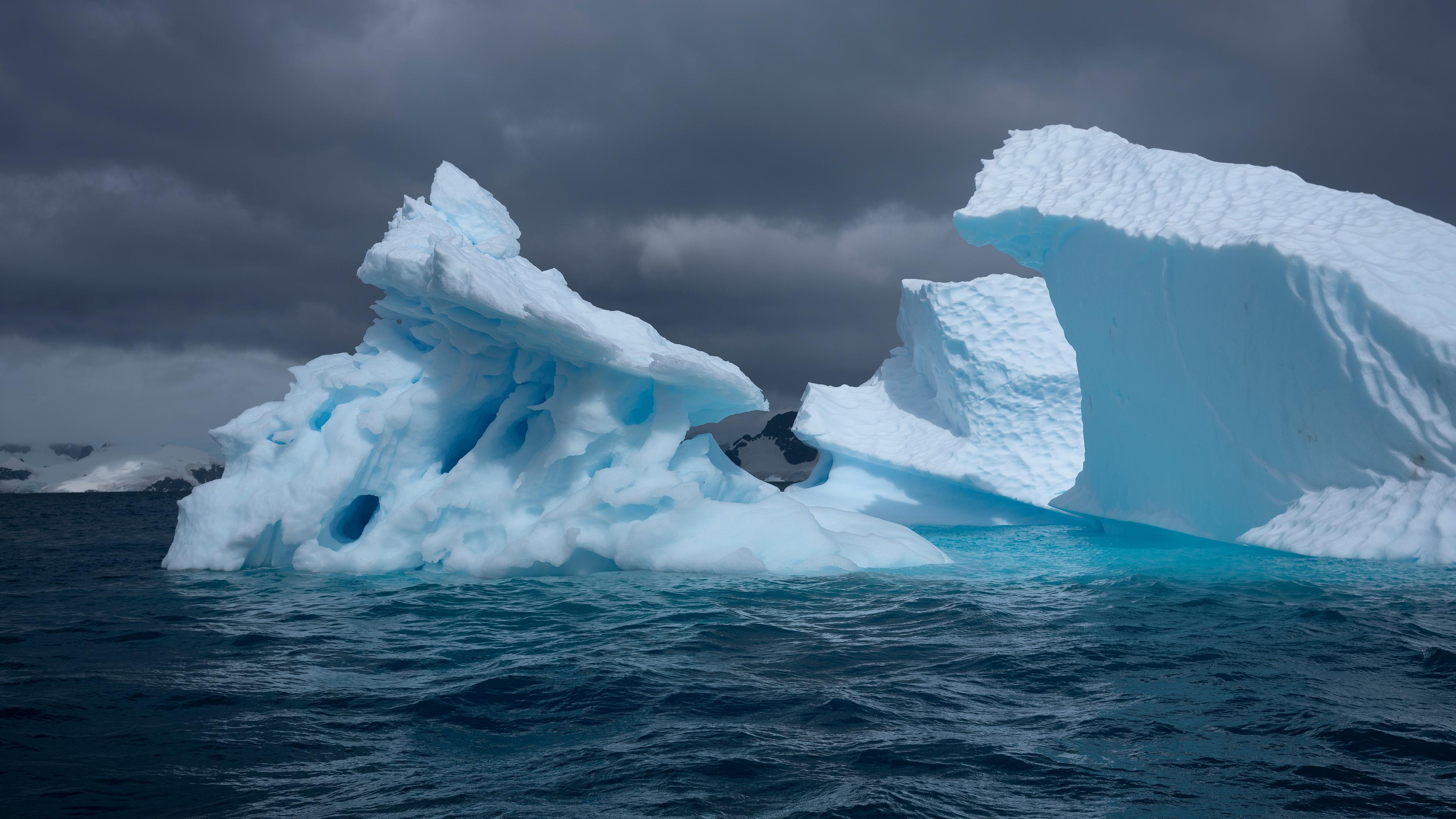 Photo of large jagged icebergs in dark ocean waters under a cloudy sky.