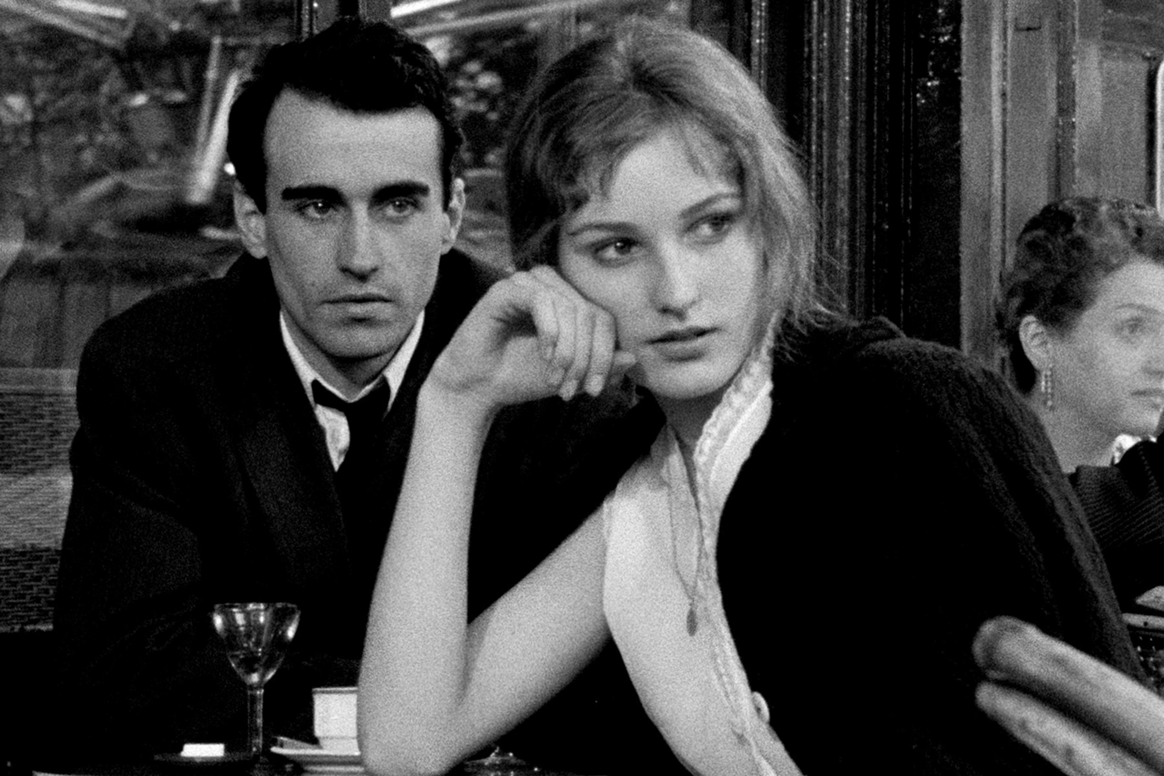 Black and white photo of a man and woman sitting at a café table in conversation, looking thoughtfully to the side.