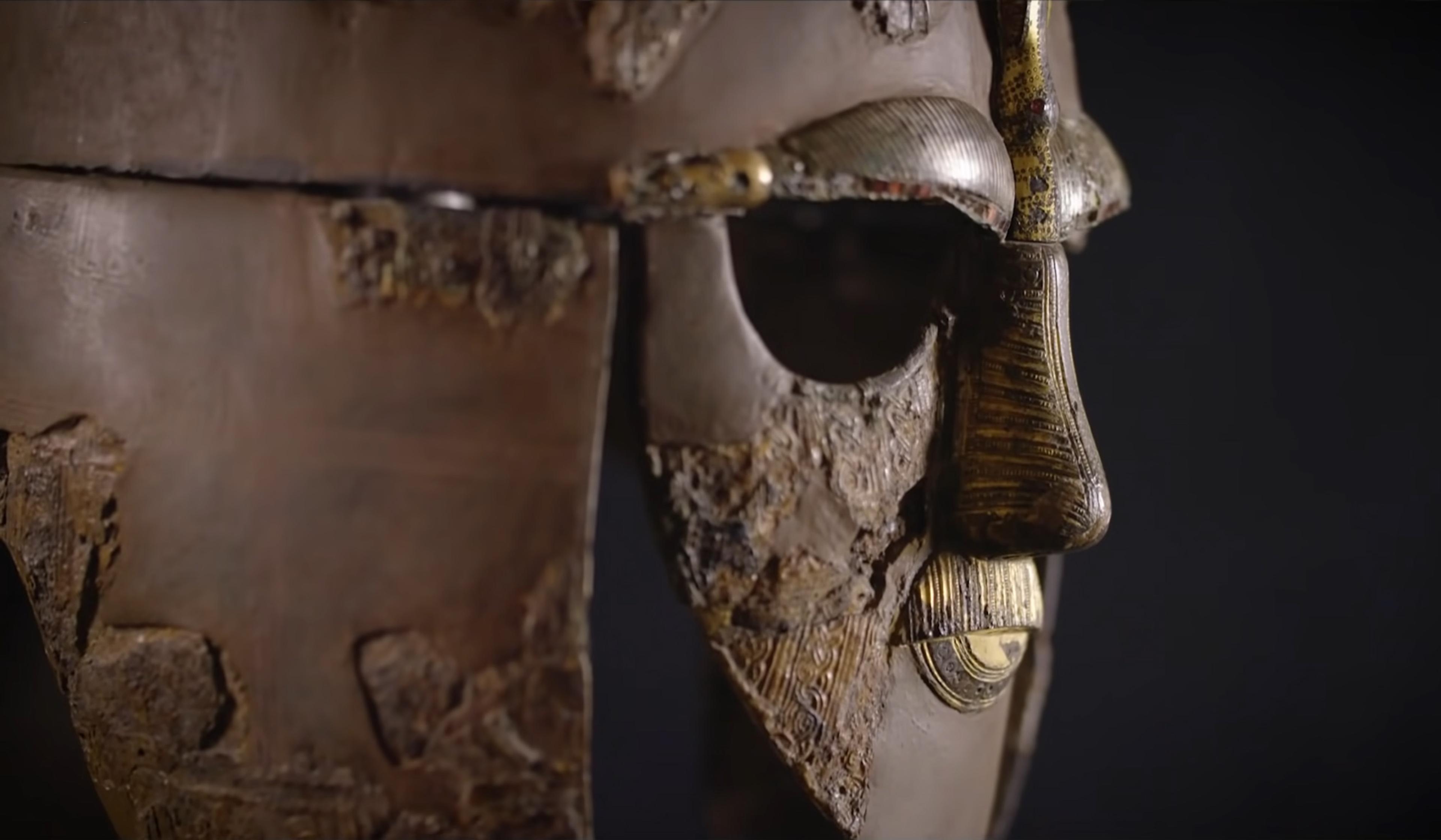 Close-up photo of an ancient helmet with detailed metalwork on a dark background.