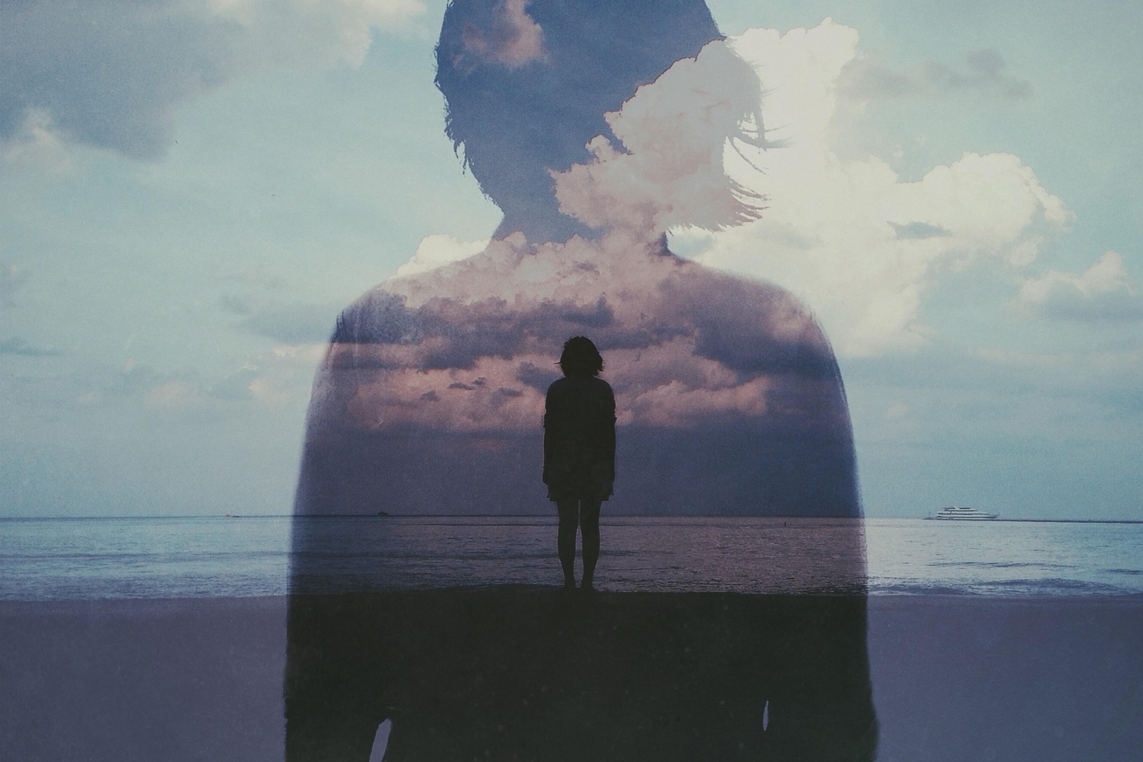 Double exposure photo of a person silhouetted against the sea with clouds overlapping their figure.