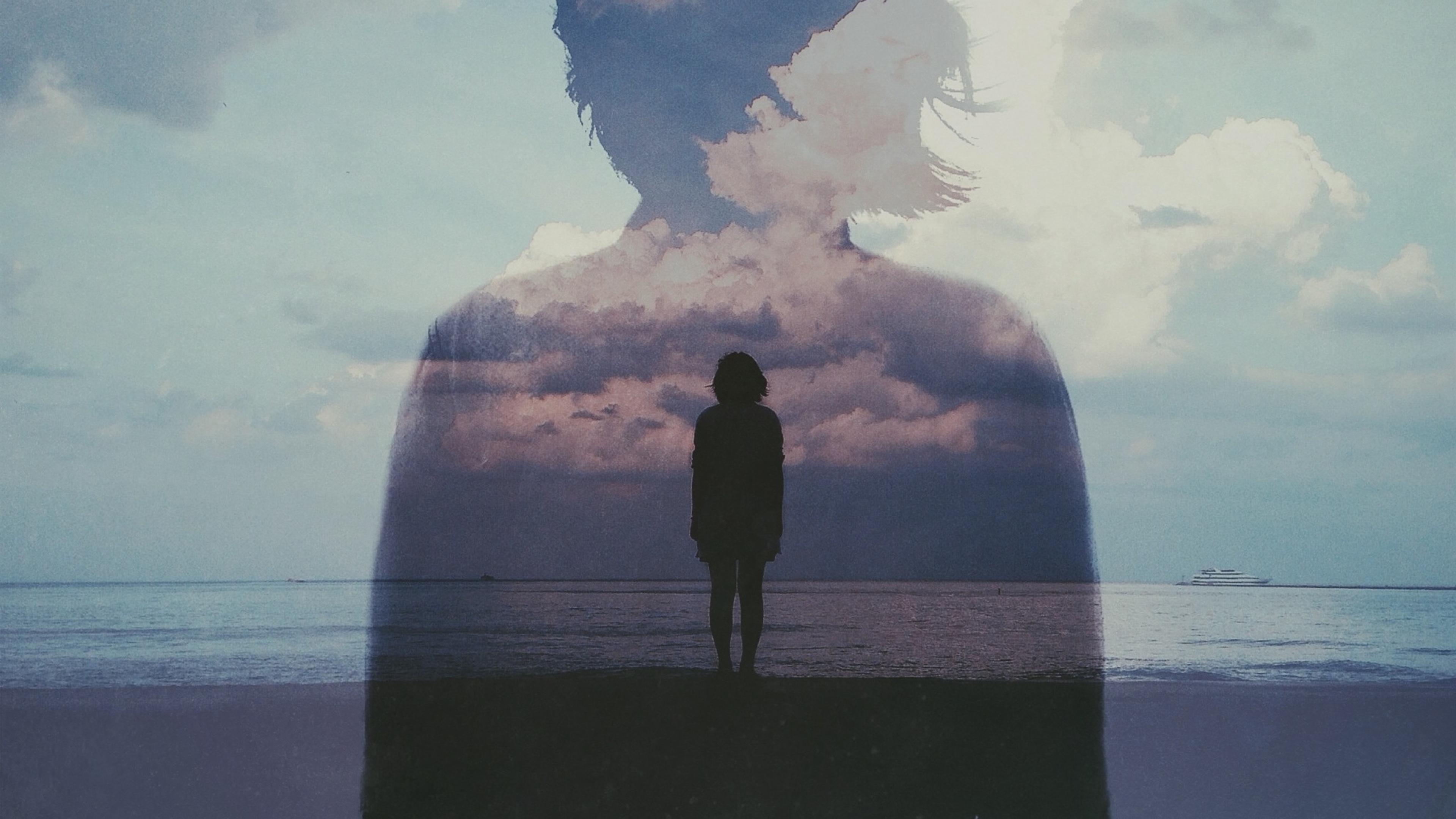 Double exposure photo of a person silhouetted against the sea with clouds overlapping their figure.