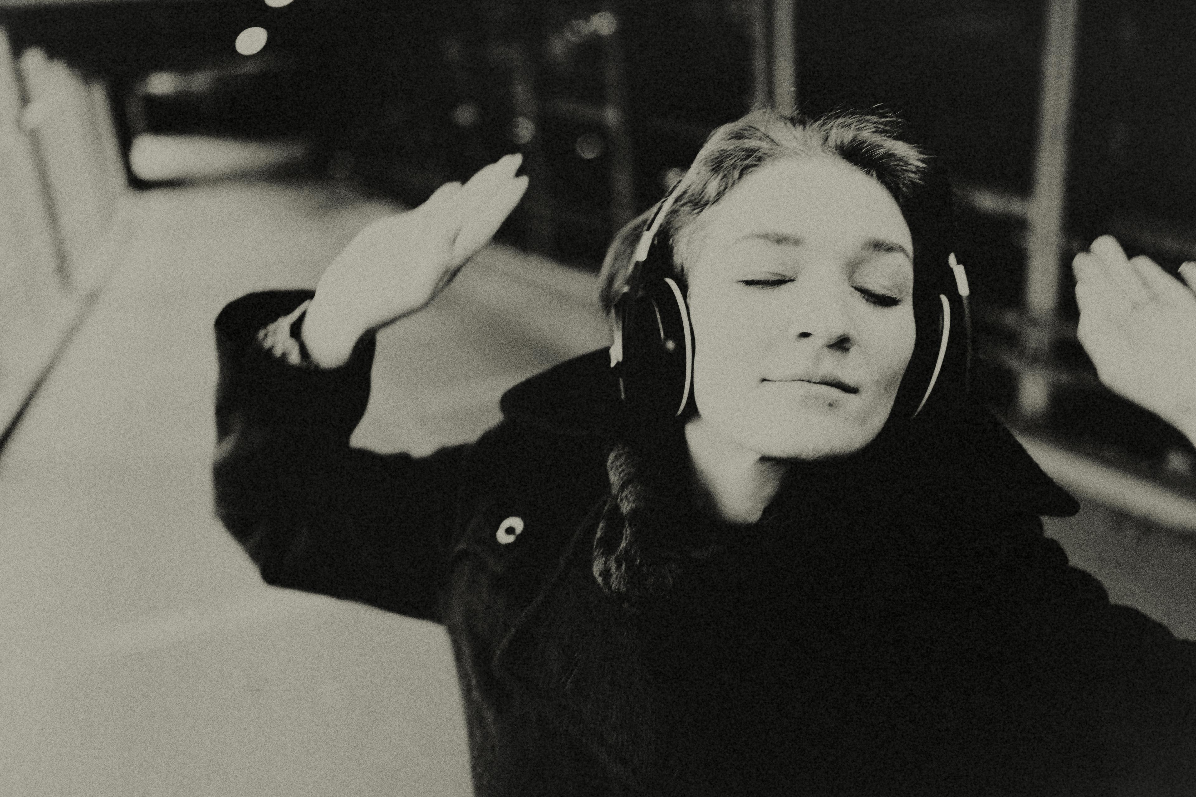 Black and white photo of a person with headphones on eyes closed hands raised appearing to enjoy music.
