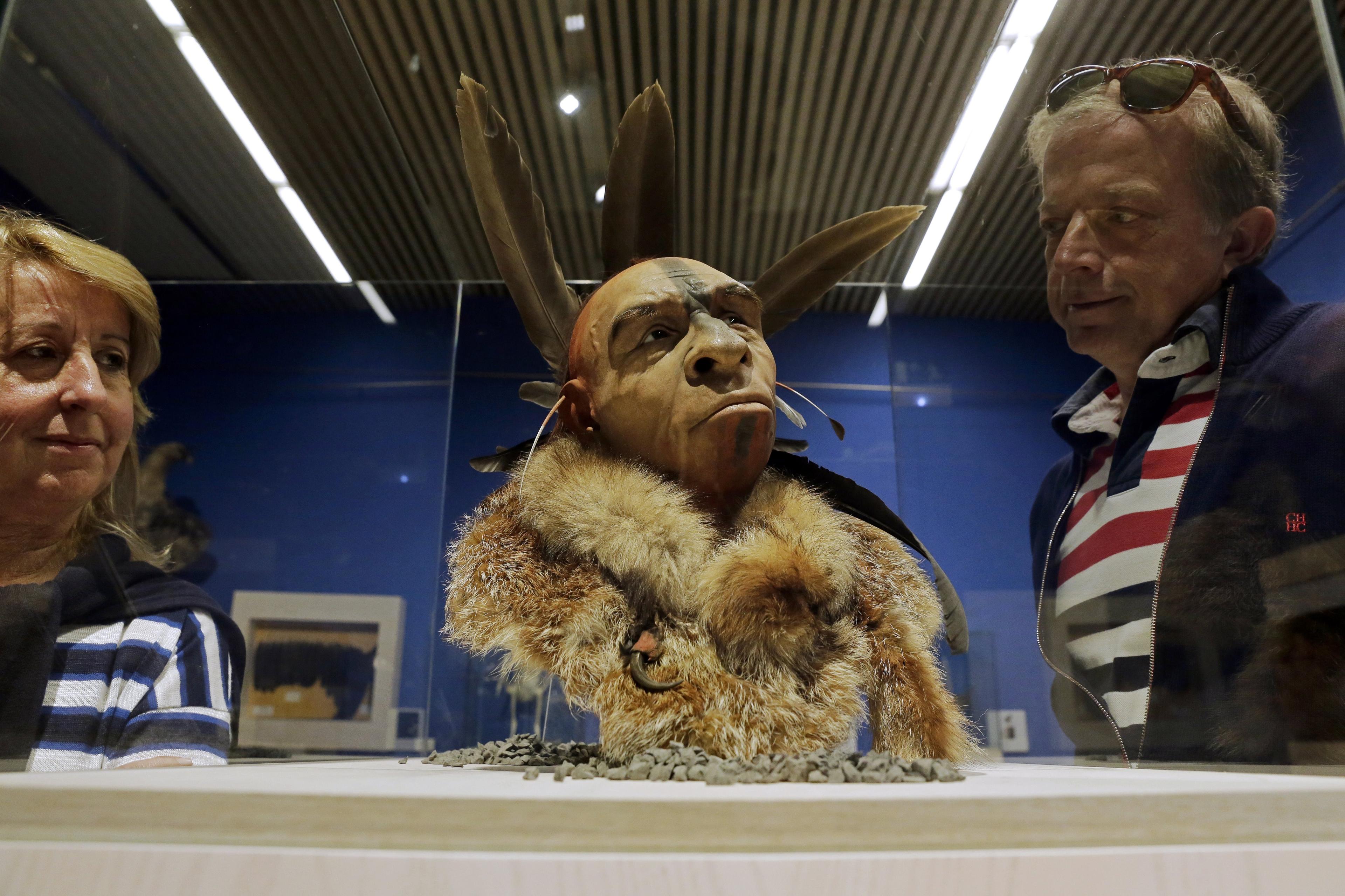 Photo of two people observing a museum display of a Indigenous head with feathers and fur in a glass case.