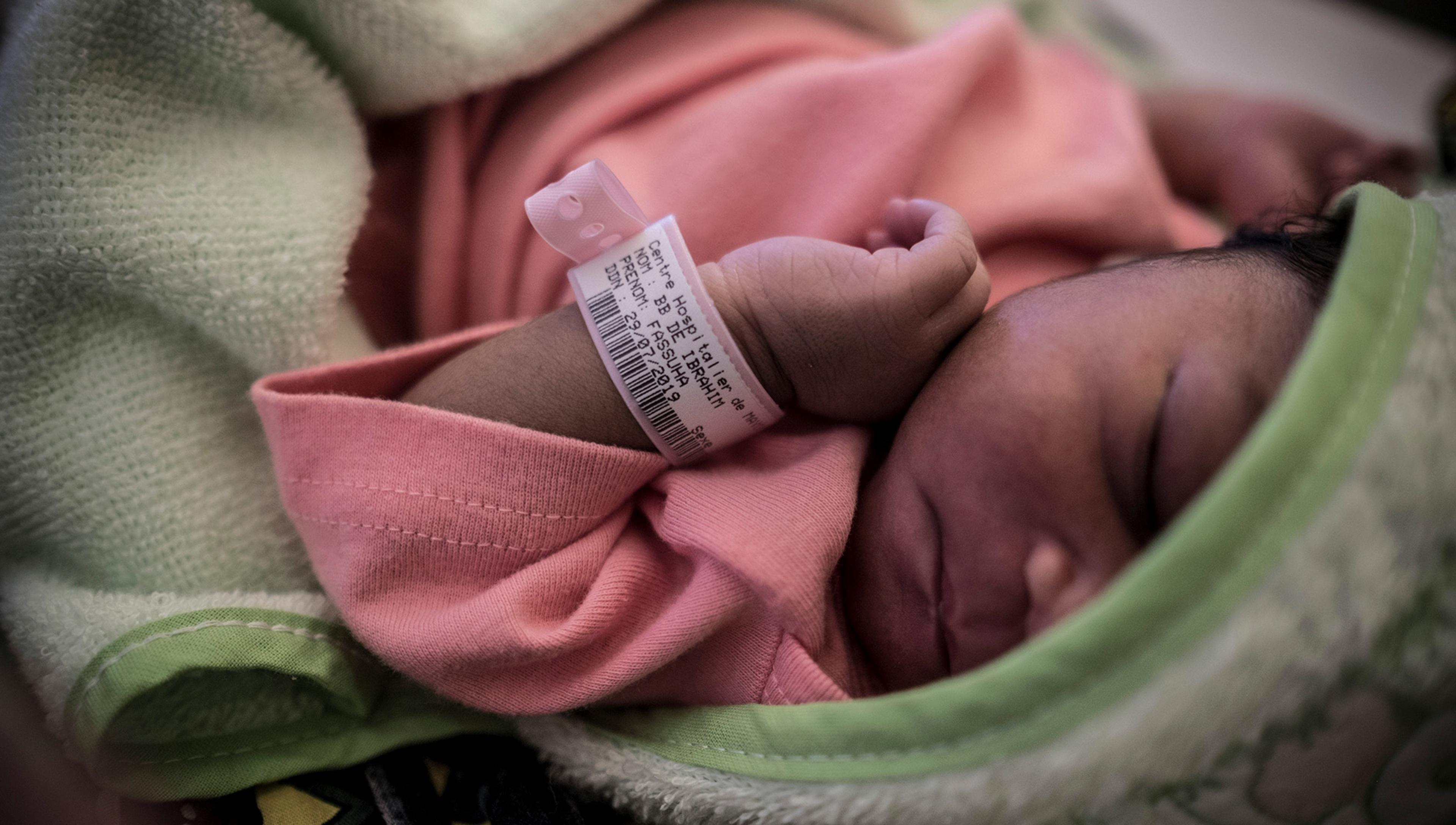 Photo of a newborn baby wearing a pink wristband and clothes wrapped in a green blanket, sleeping peacefully.