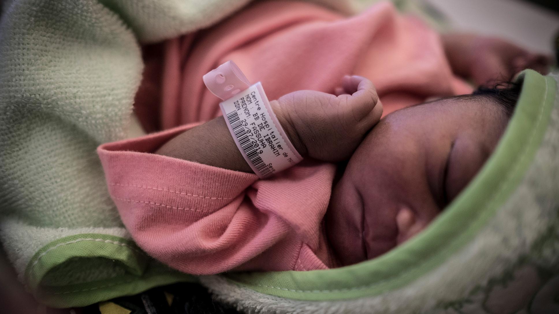 Photo of a newborn baby wearing a pink wristband and clothes wrapped in a green blanket, sleeping peacefully.