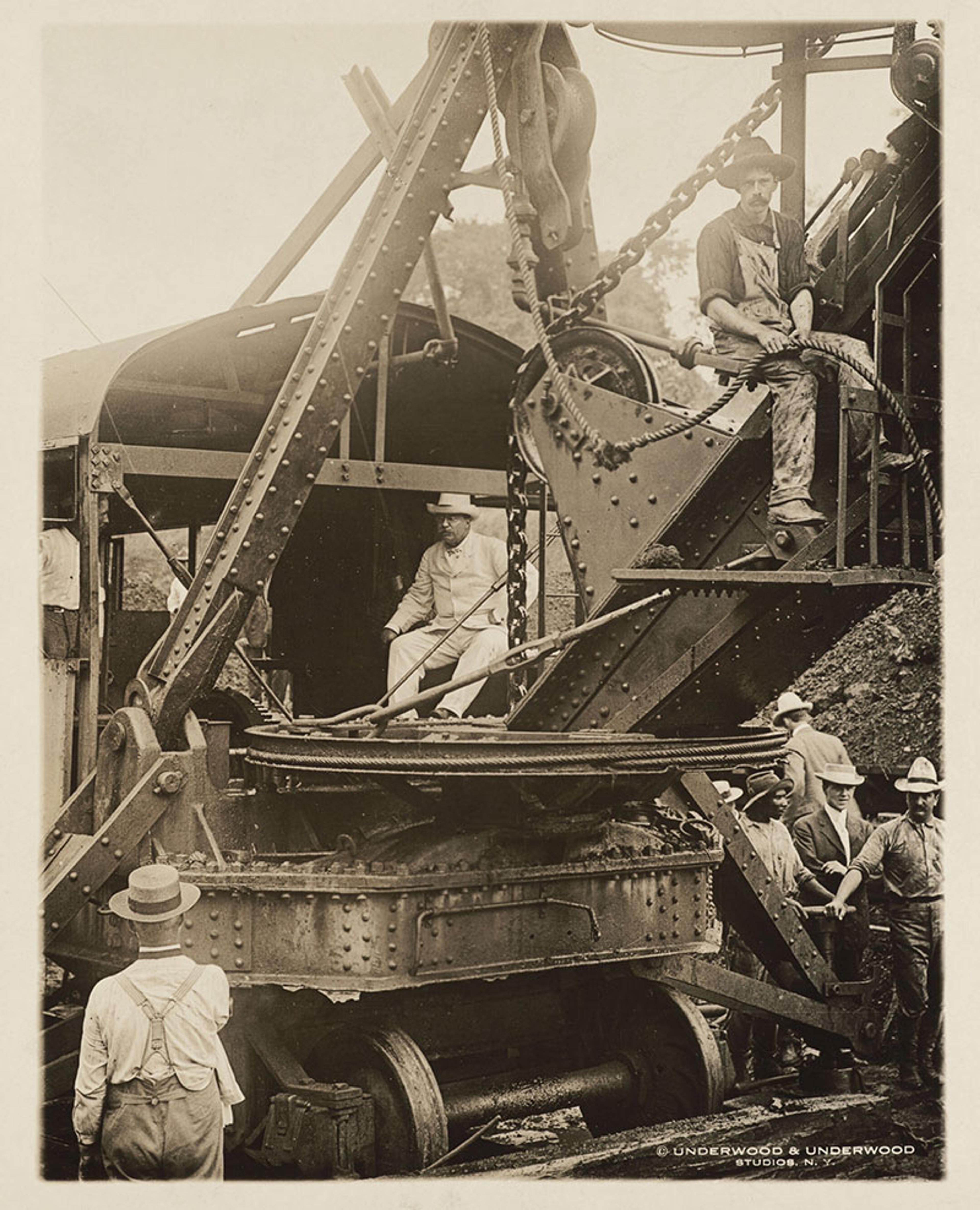 Historic photo of workers operating a steam shovel with onlookers in hats and overalls, early 20th century construction site.