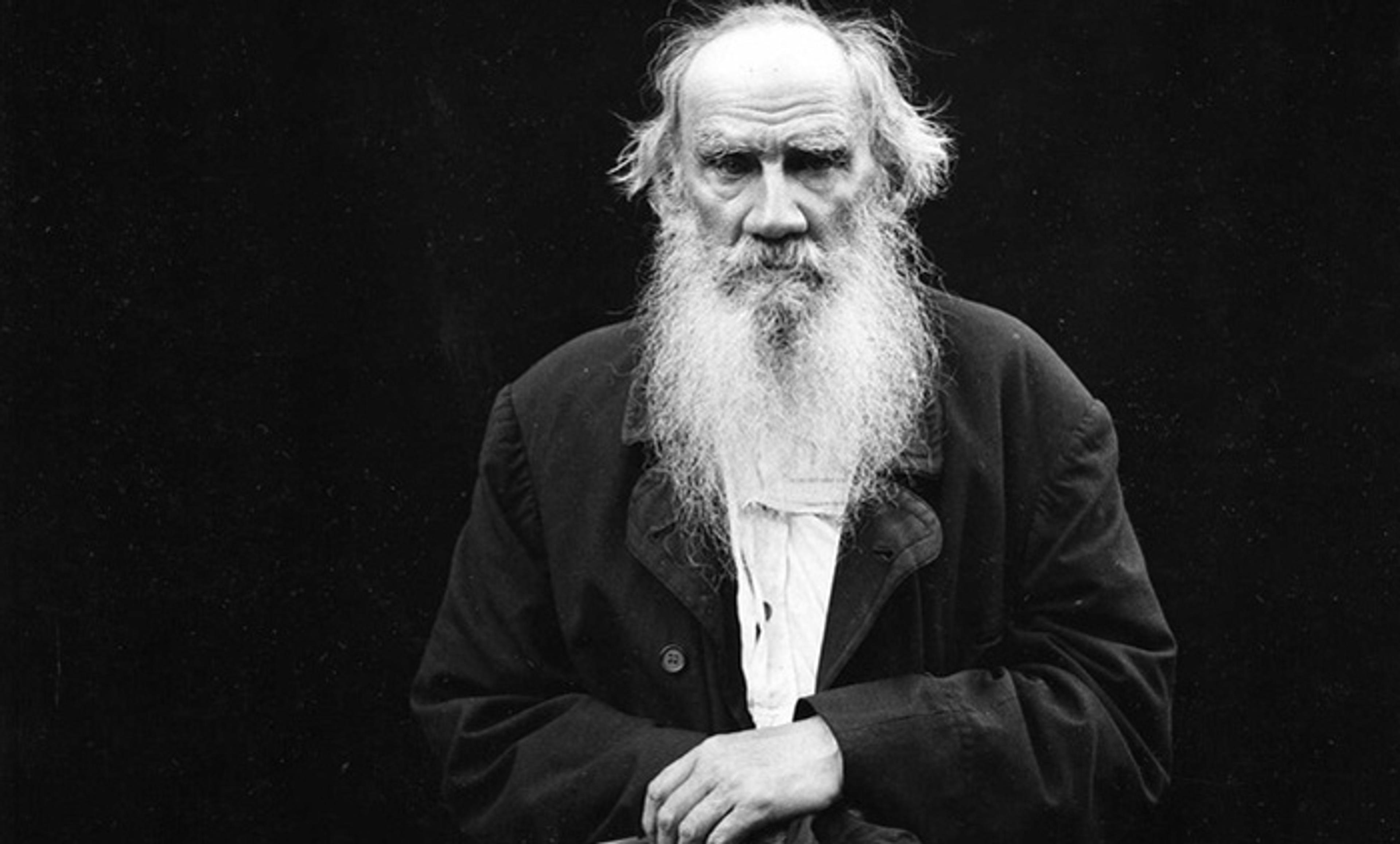 Vintage photo of an elderly man with a long beard in dark clothing looking at the camera against a dark background.