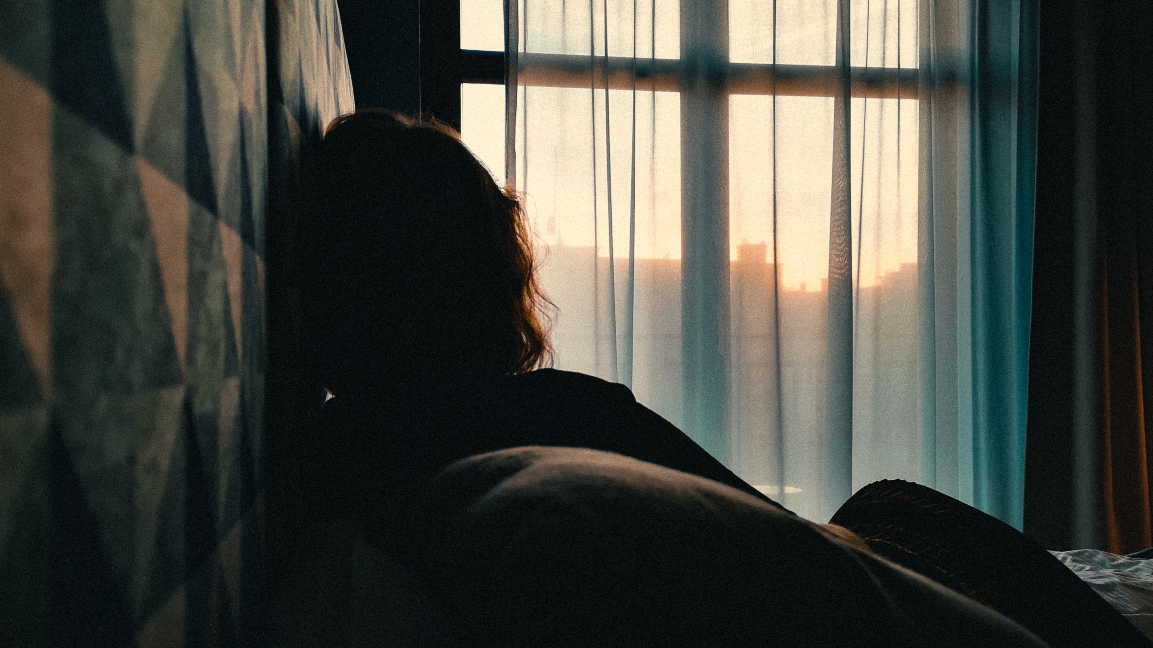 Silhouette of a person looking out a window at sunset with geometric patterned wall. Photo with moody lighting.