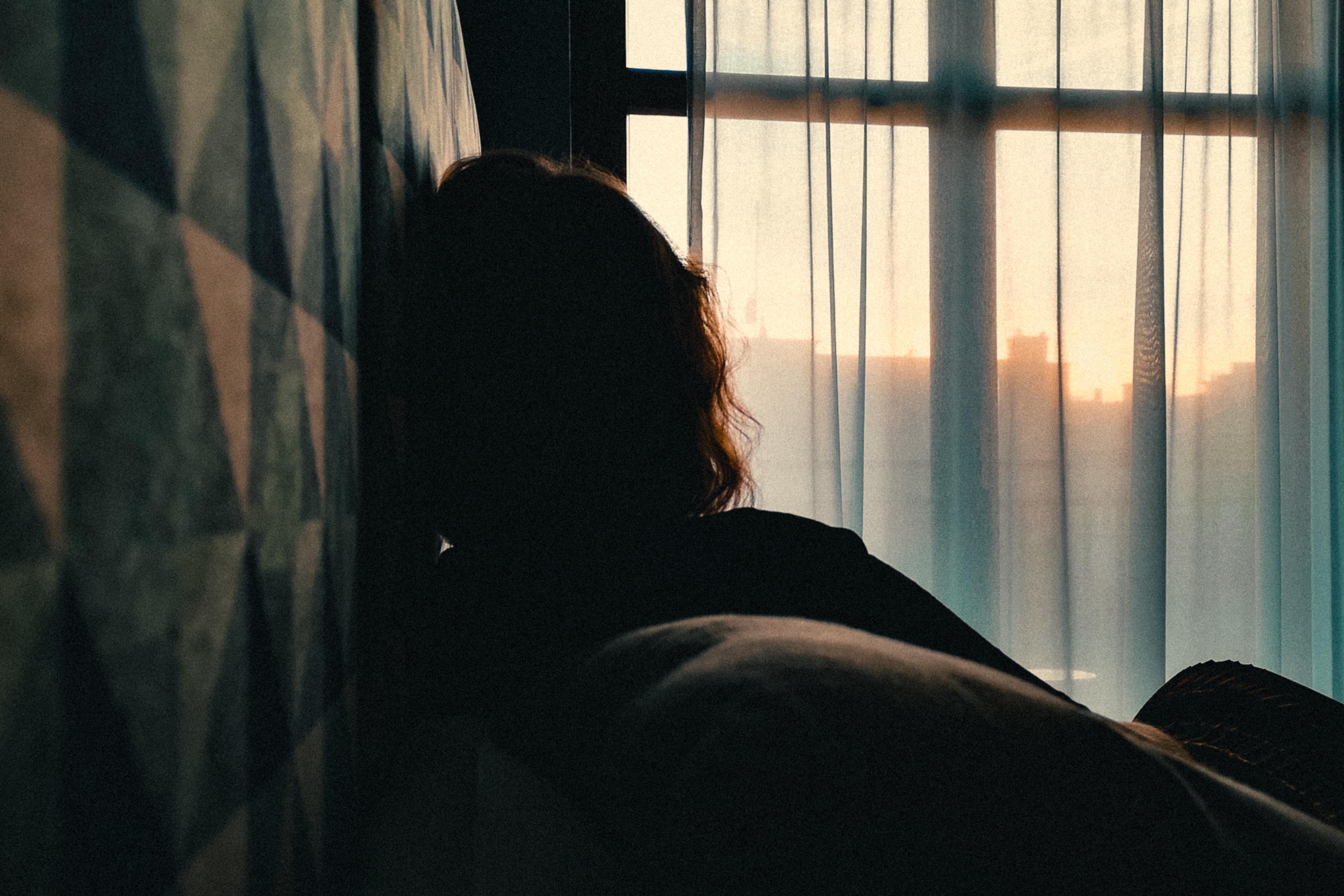 Silhouette of a person looking out a window at sunset with geometric patterned wall. Photo with moody lighting.