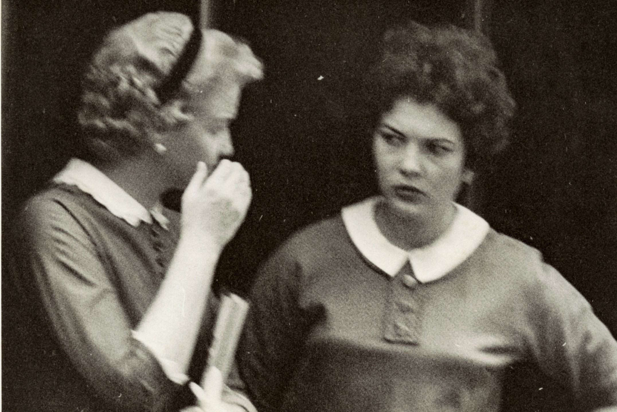 Black and white photo of two women from the 1950s, one whispering to the other.